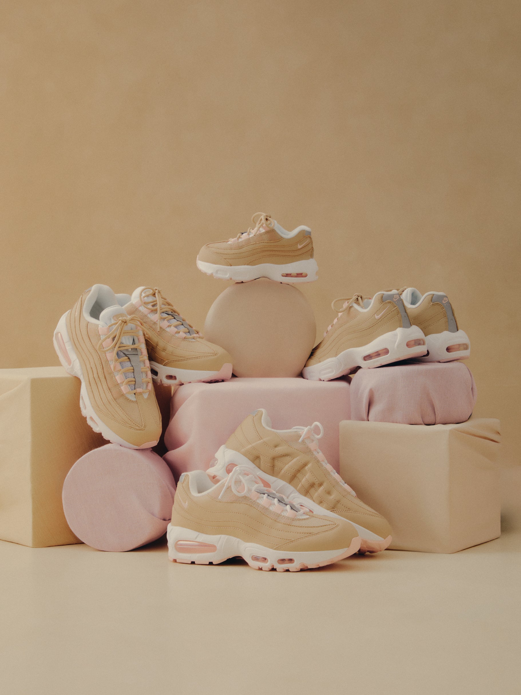 Nike Air Max 95 sneakers in tan with pink accents, four pairs styled on pastel beige and pink geometric blocks and props