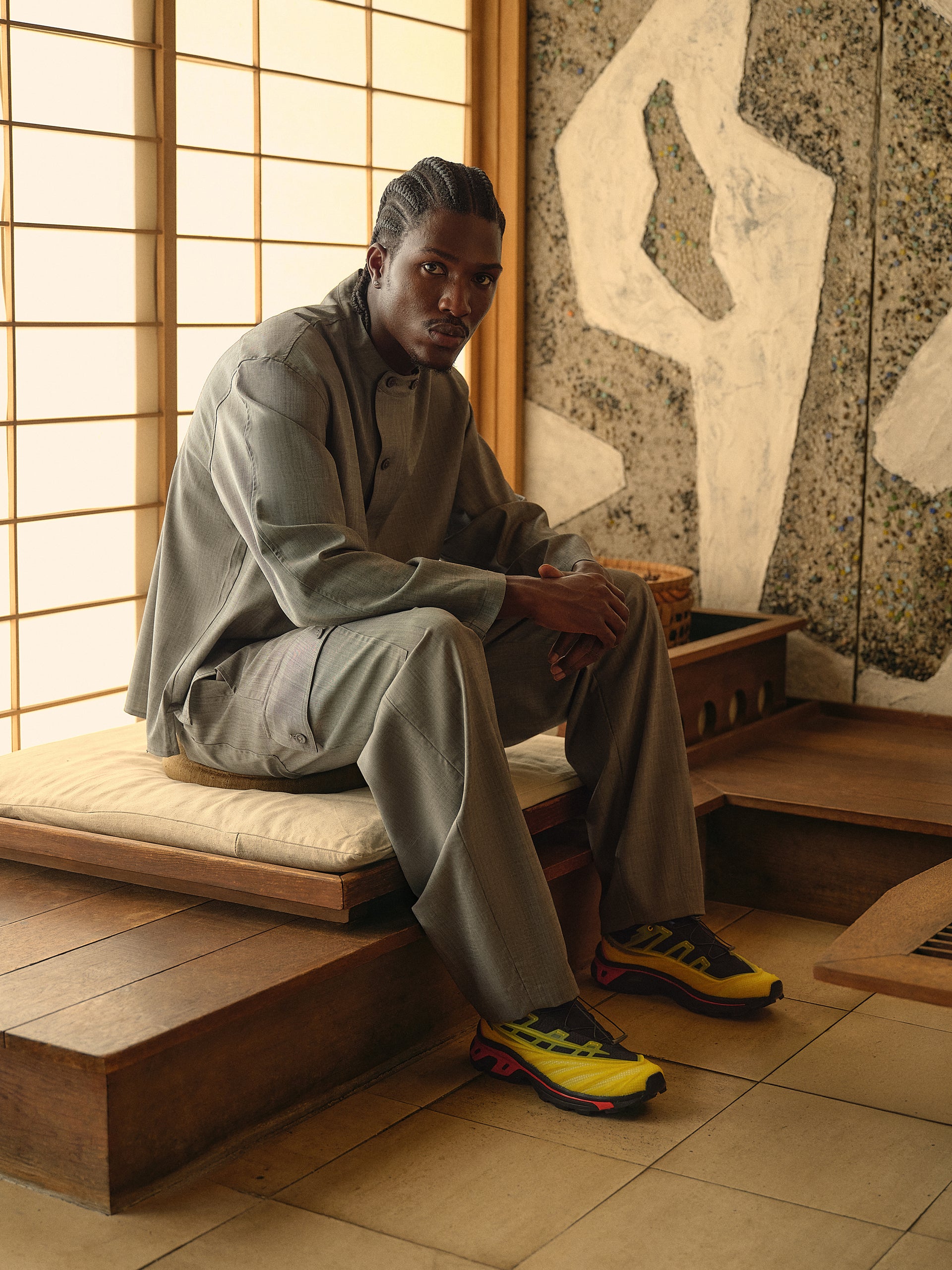 Man seated in a Japanese-style room in a grey suit and yellow-black-red Salomon XT sneakers