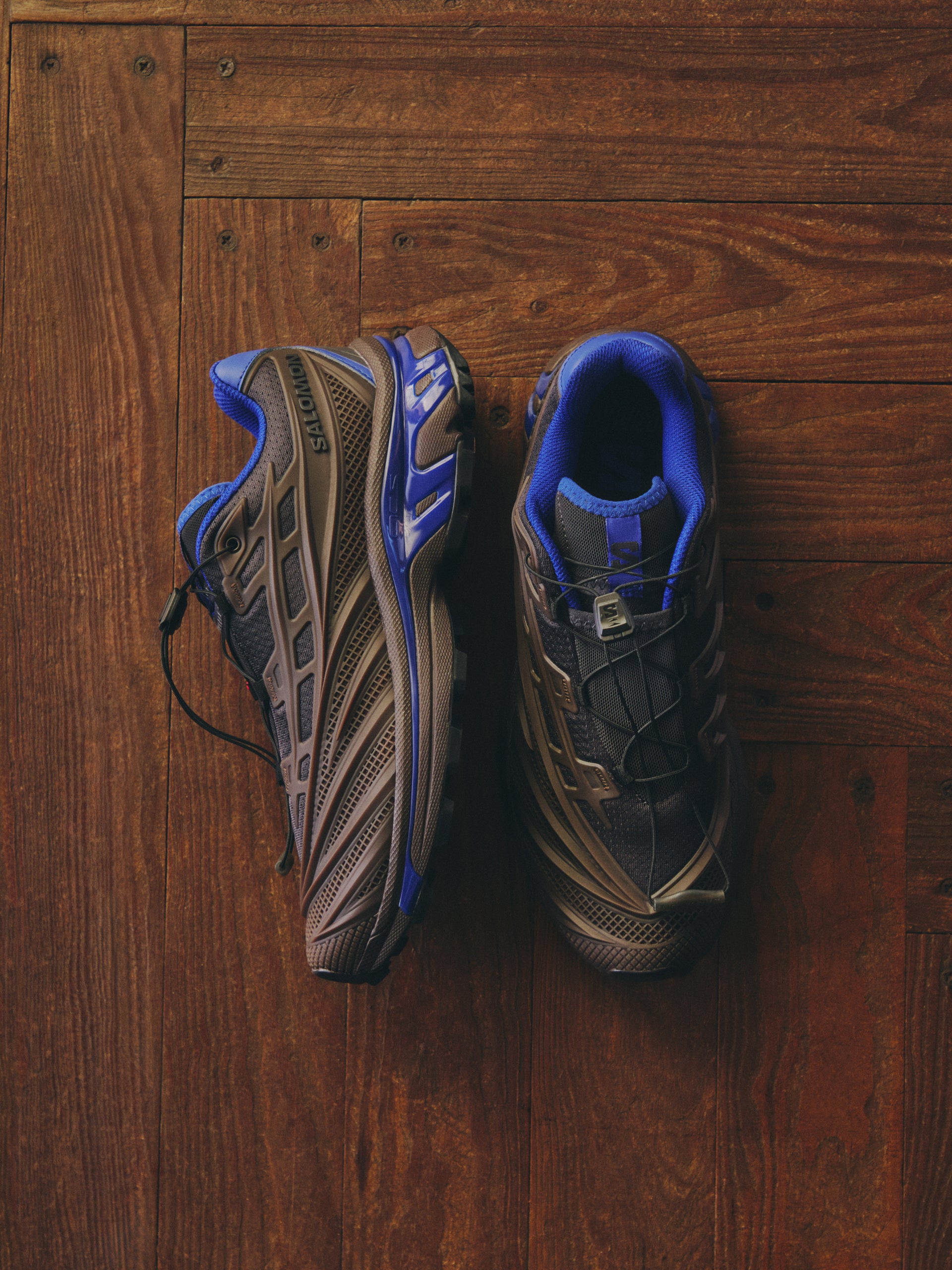 Pair of Salomon XT sneakers in brown and grey with blue accents, top and side view on dark wood floor