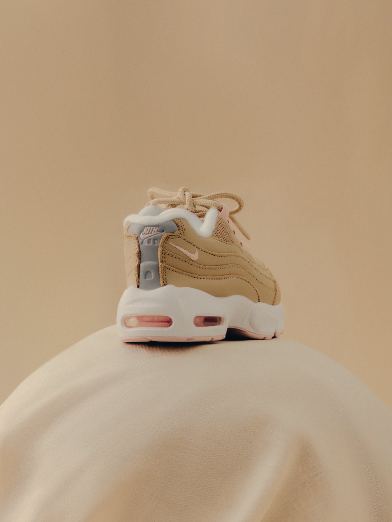 Kith x Nike Air Max 95 in tan and pink, rear heel view with KITH Air branding, on cream fabric