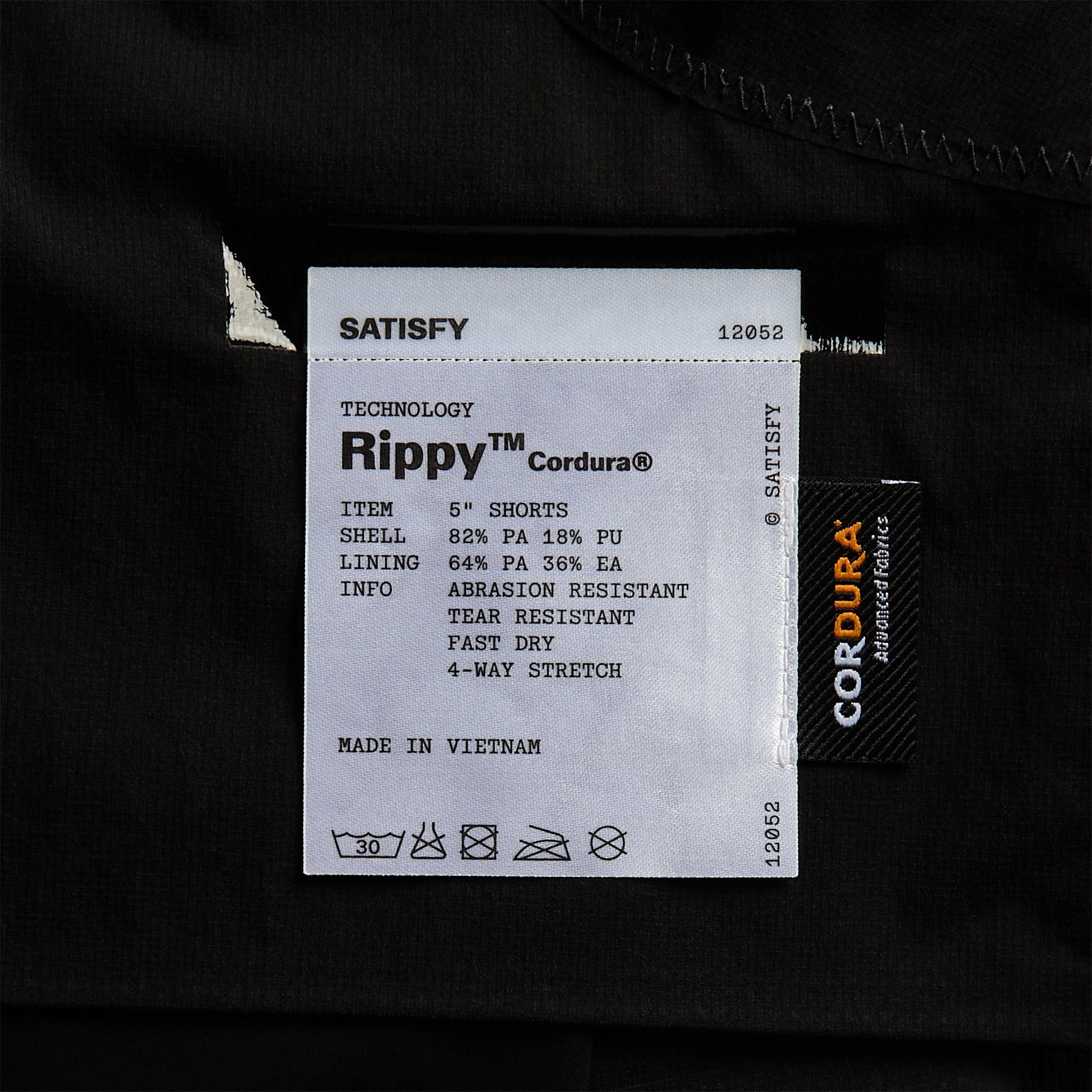 Close-up of the sewn-in Satisfy Rippy Cordura care label noting abrasion-resistant, tear-resistant, fast-dry 4-way stretch fabric