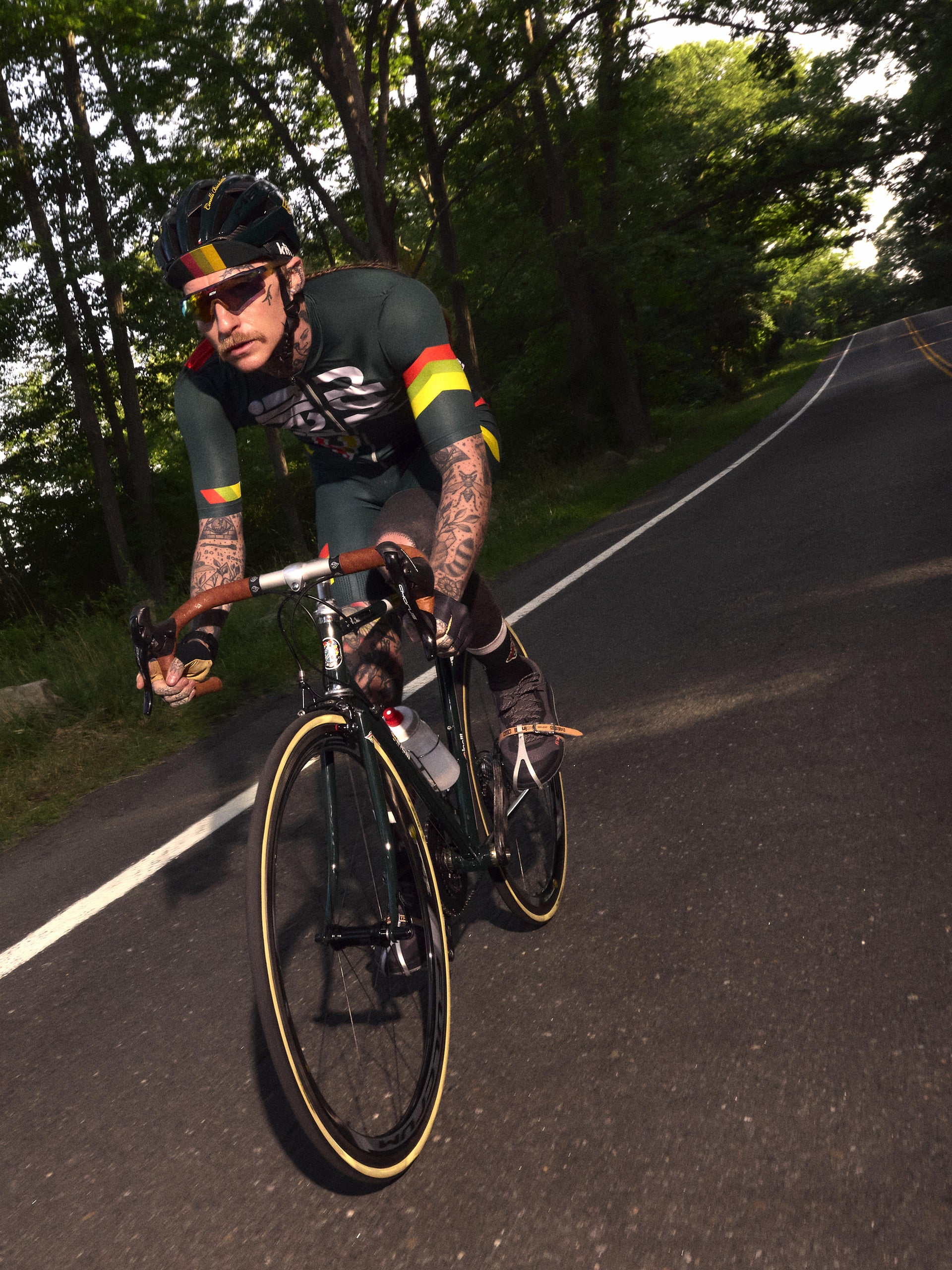 Cyclist speeding along a tree-lined road in green Cinelli x Kith kit, motion-blur action shot
