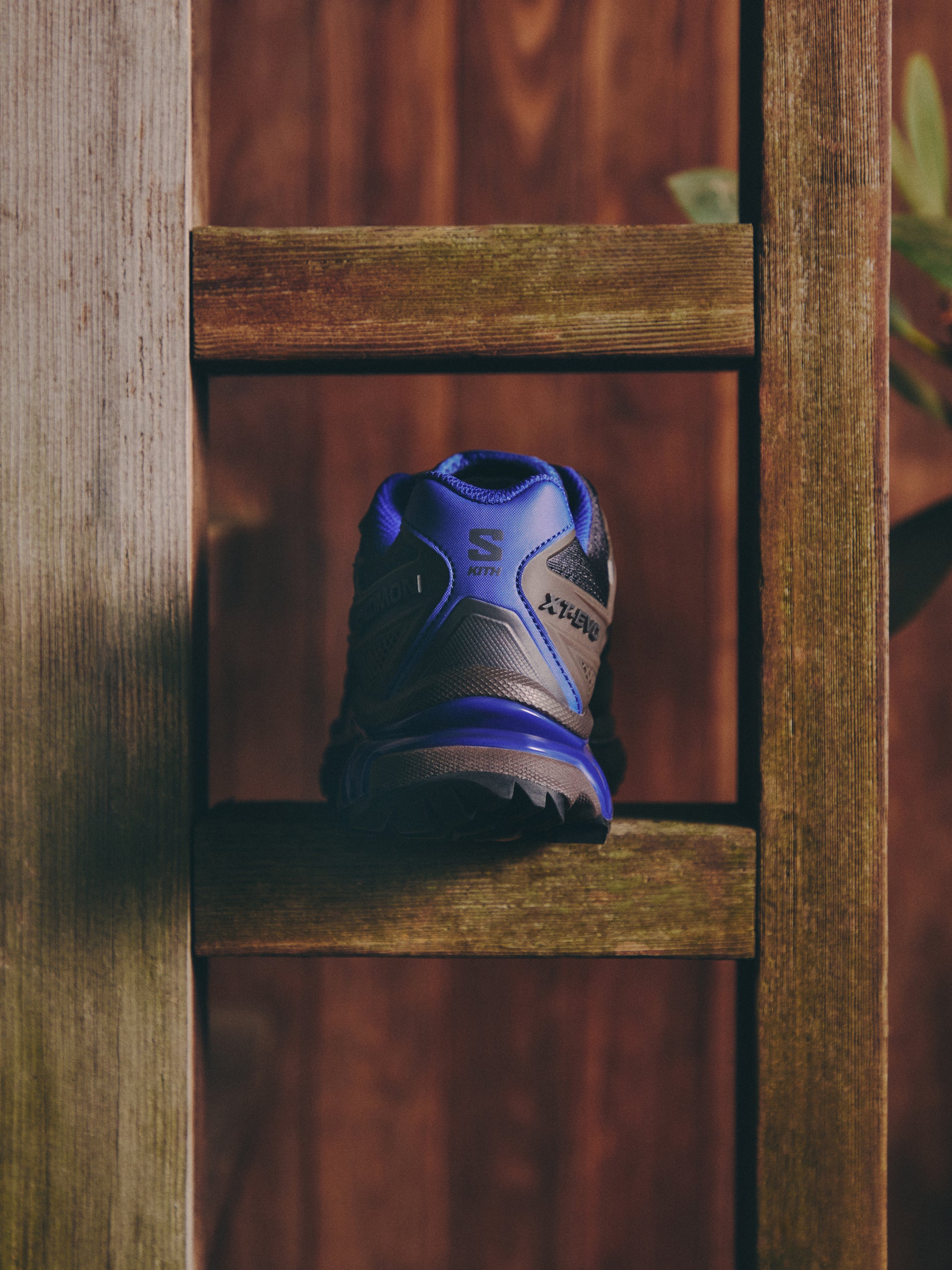 Salomon XT-EVO sneaker in blue and brown, heel view with Kith branding, on a wood fence rung