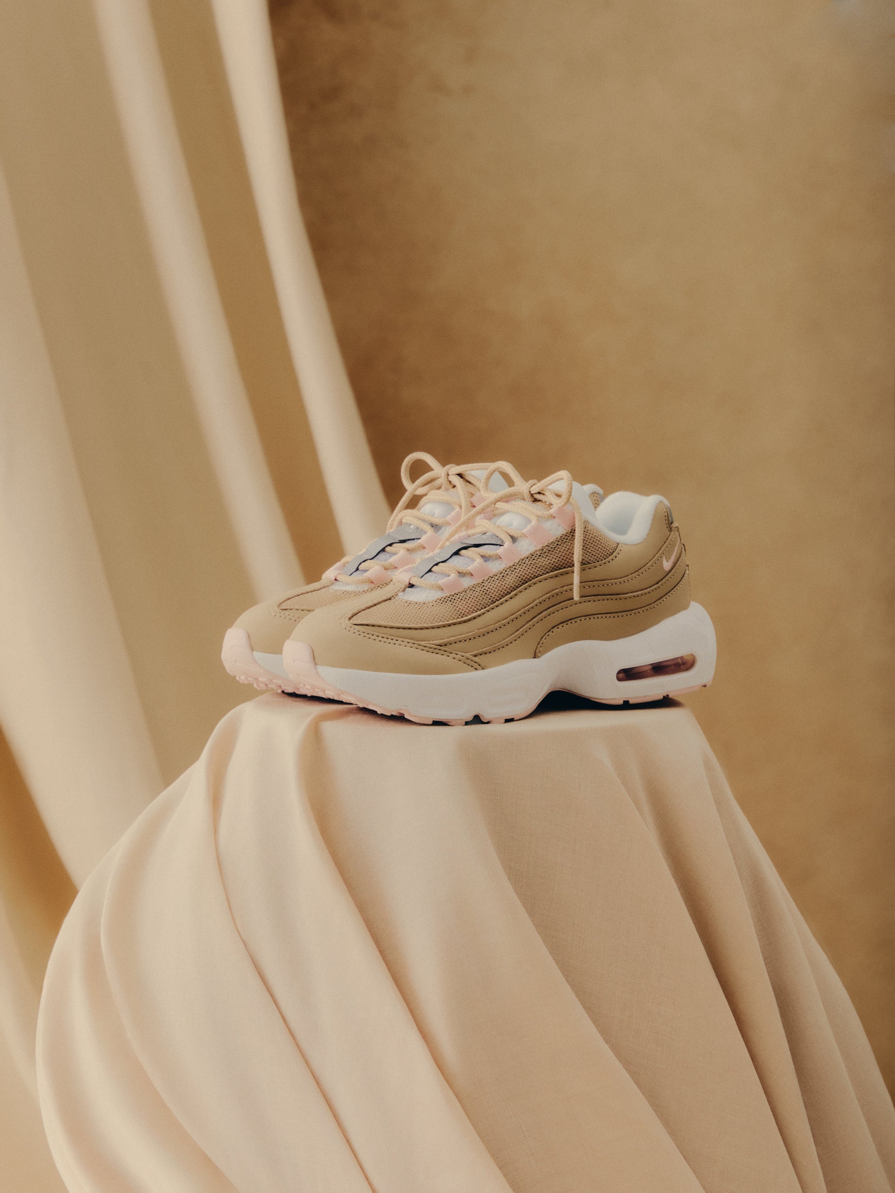 Kith x Nike Air Max 95 pair in tan and pink, front three-quarter view on draped cream fabric