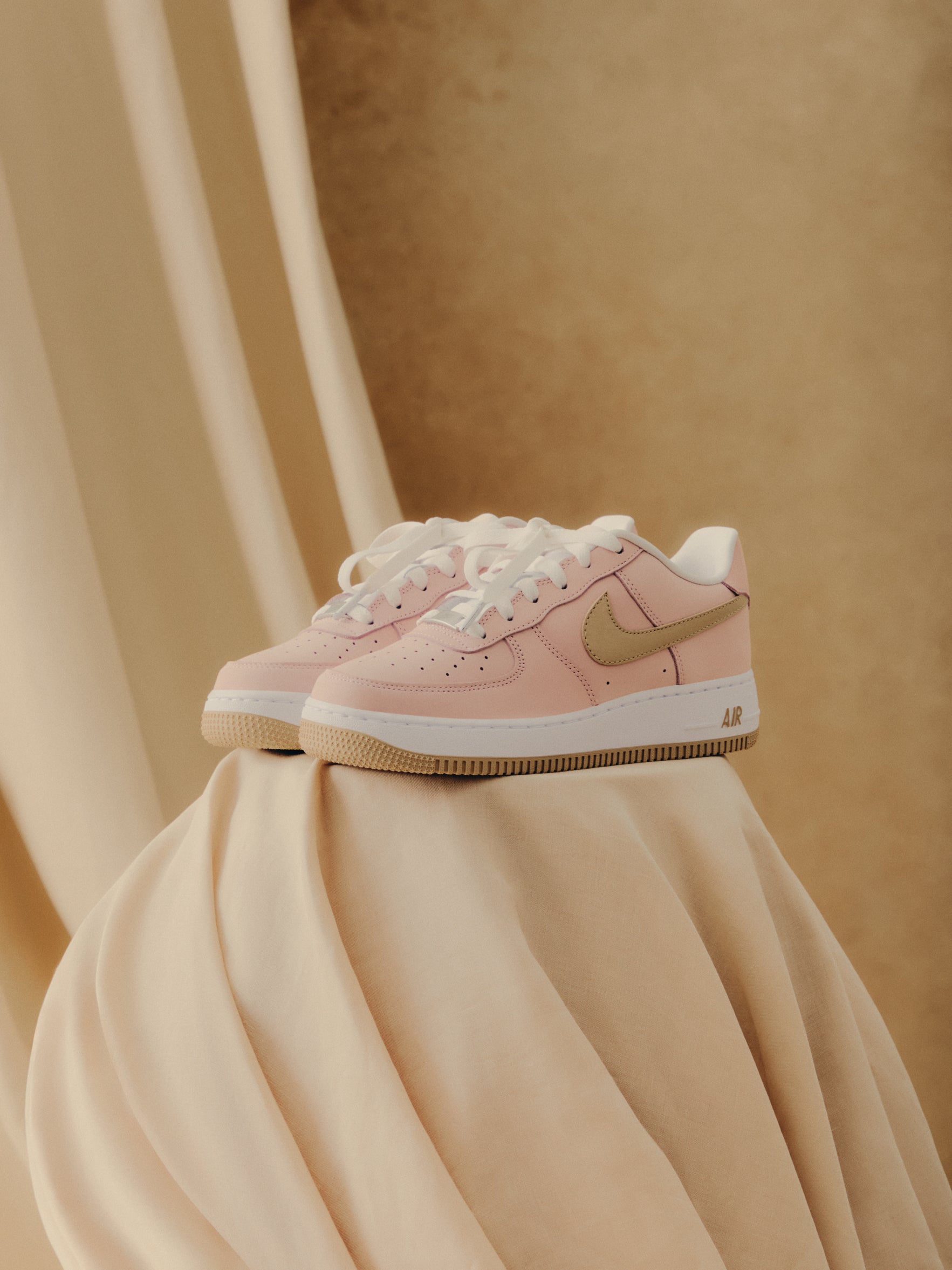Kith x Nike Air Force 1 Low pair, pink with tan Swoosh and gum sole, front angle on cream fabric