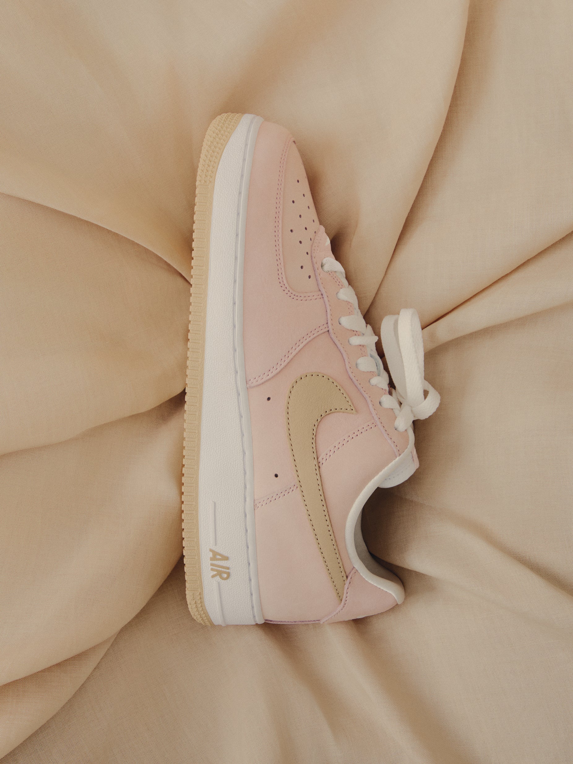Kith x Nike Air Force 1 Low, pink with tan Swoosh and gum sole, lateral side view on beige fabric