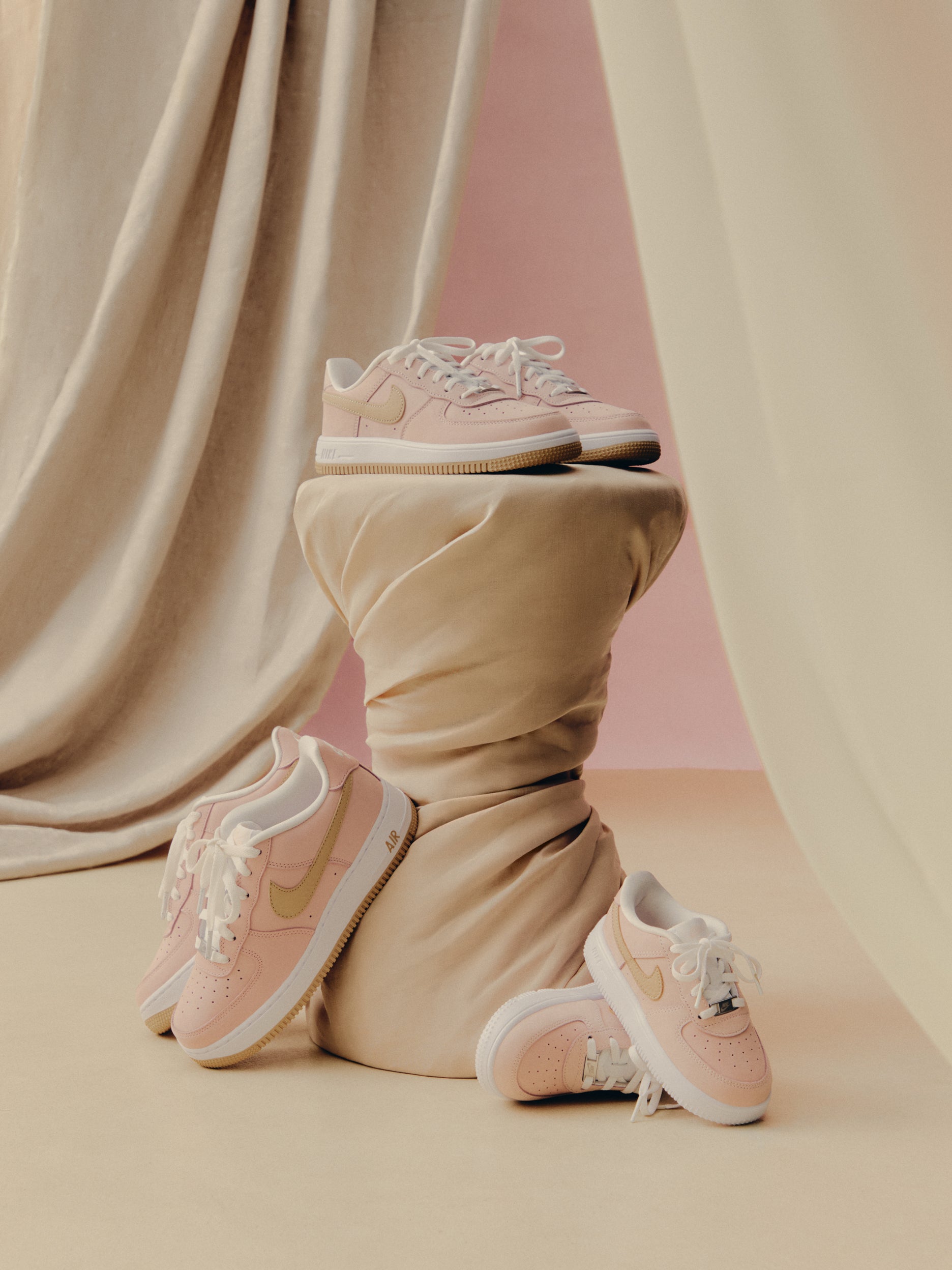 Kith x Nike Air Force 1 Low sneakers, pink with tan Swoosh, arranged on twisted beige fabric