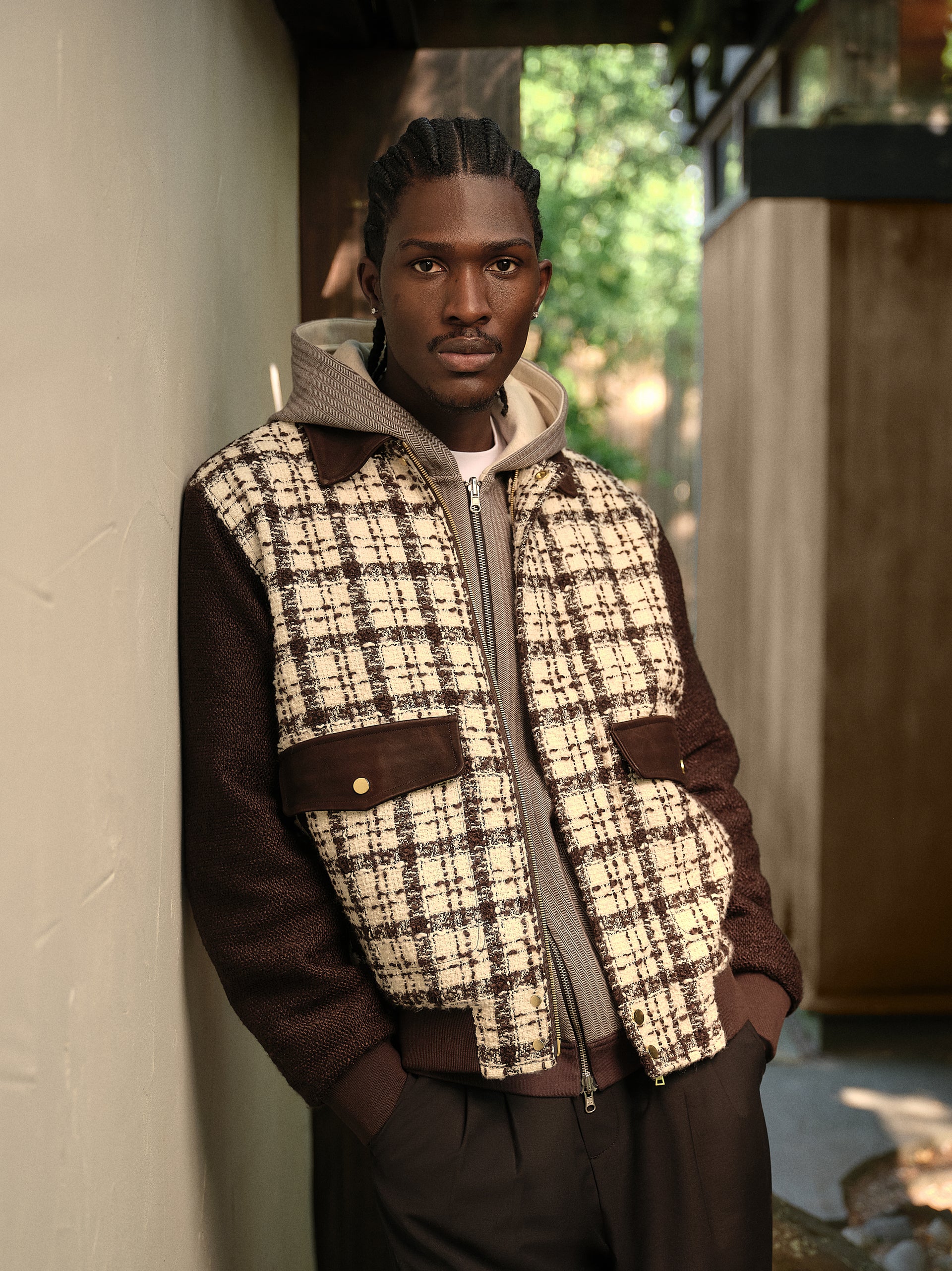 Model in profile wearing wire glasses and a patchwork blue-stripe chambray overshirt over a navy shirt, in a palm garden