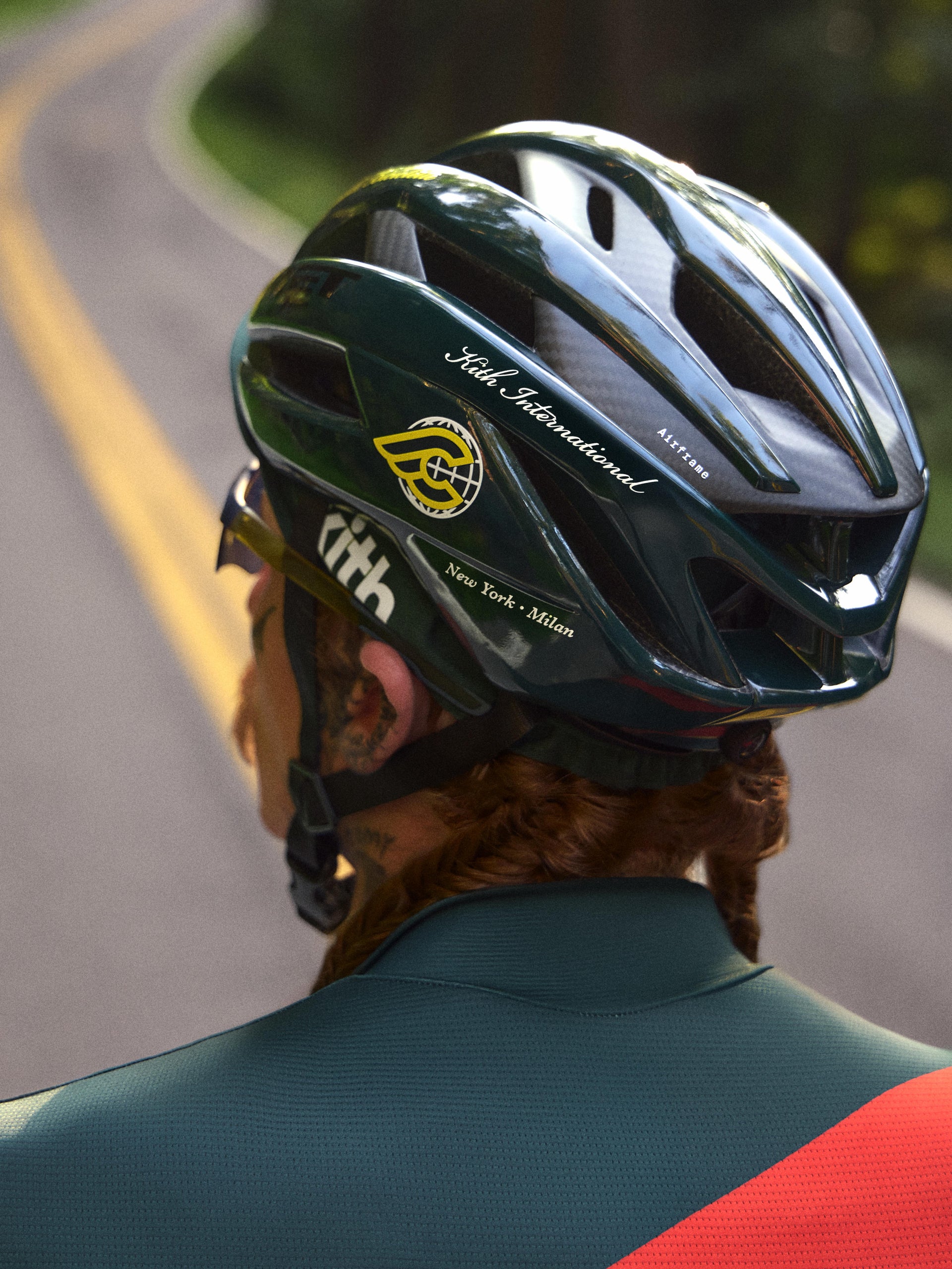 Rear view of cyclist in a green MET Airframe helmet with Kith International decals over a green jersey on a road
