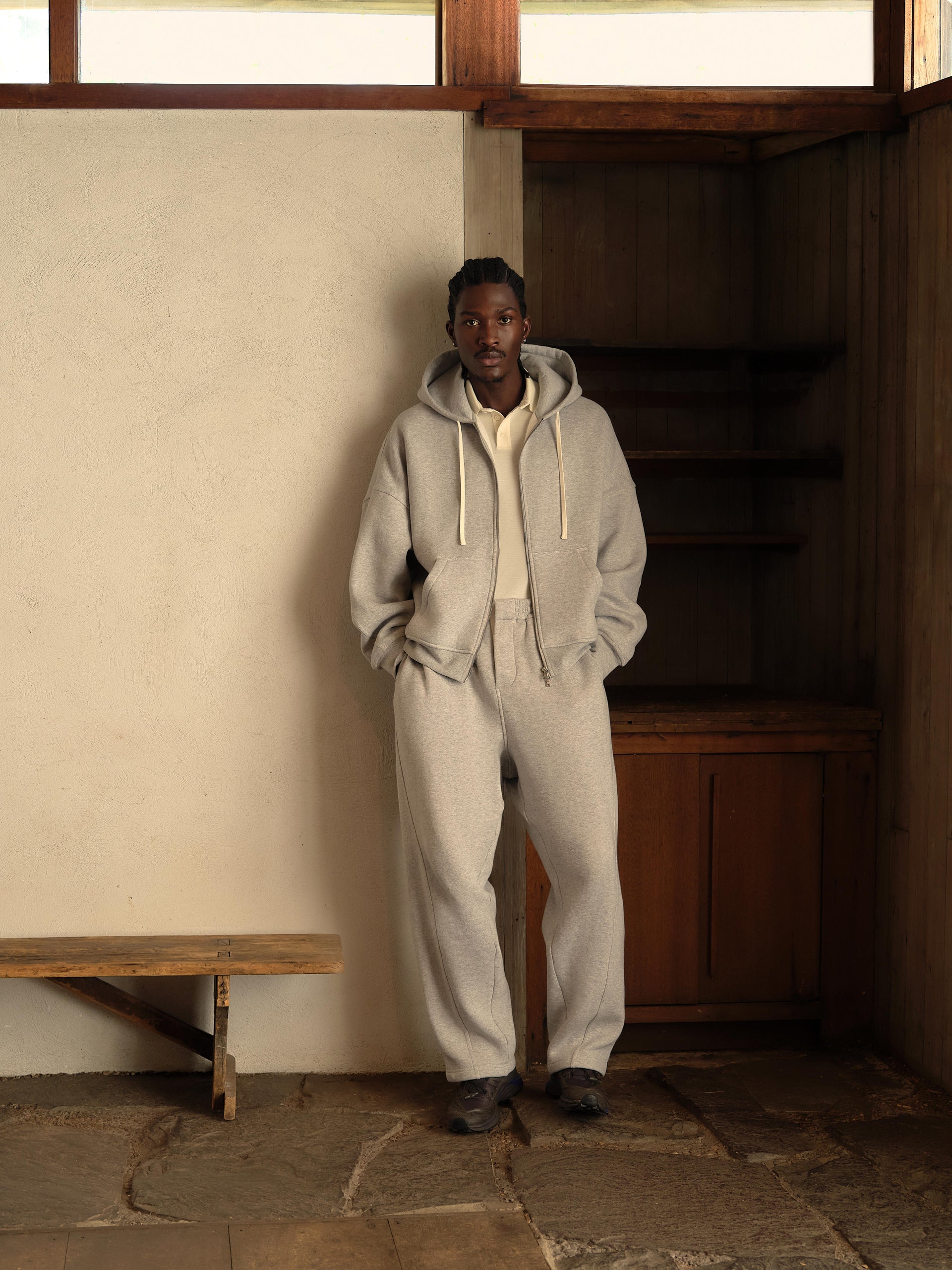 Kith fall editorial: model in a heather grey zip hoodie and matching sweatpants over a cream polo against a plaster wall