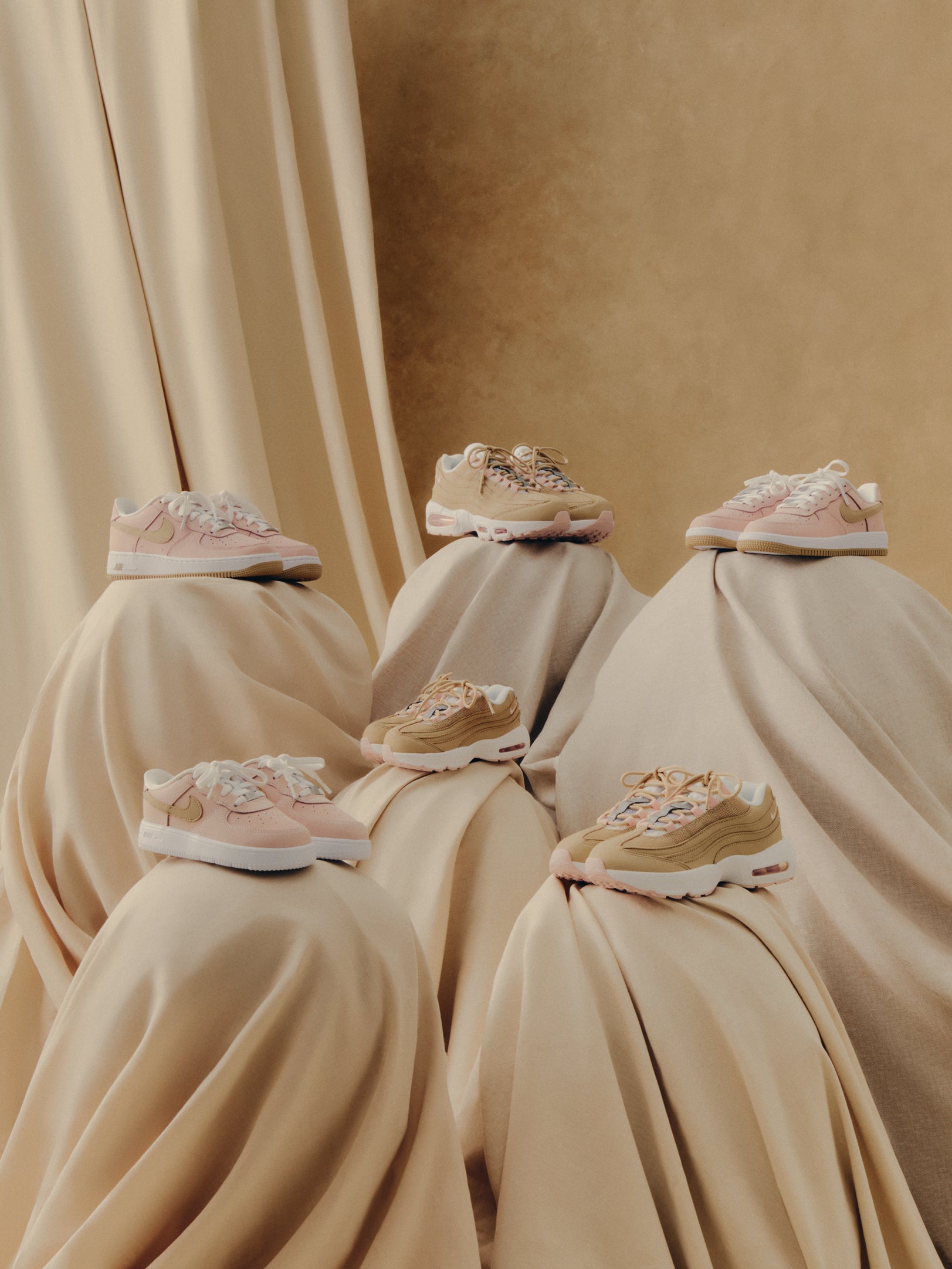 Kith x Nike collection of pink and tan Air Force 1 and Air Max 95 sneakers on draped beige fabric