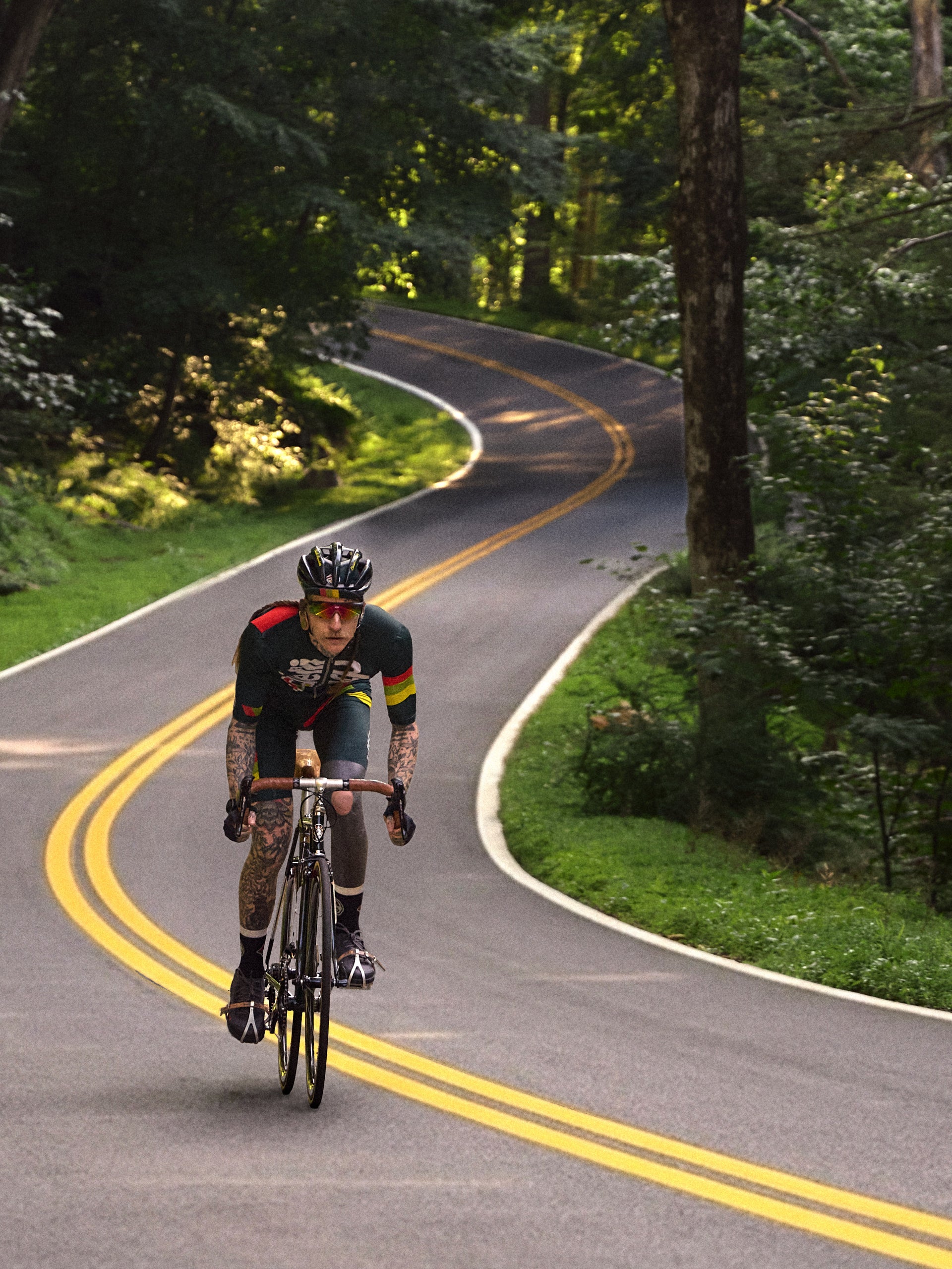 Cyclist in green striped jersey riding a vintage road bike toward camera on a winding forest road, action shot