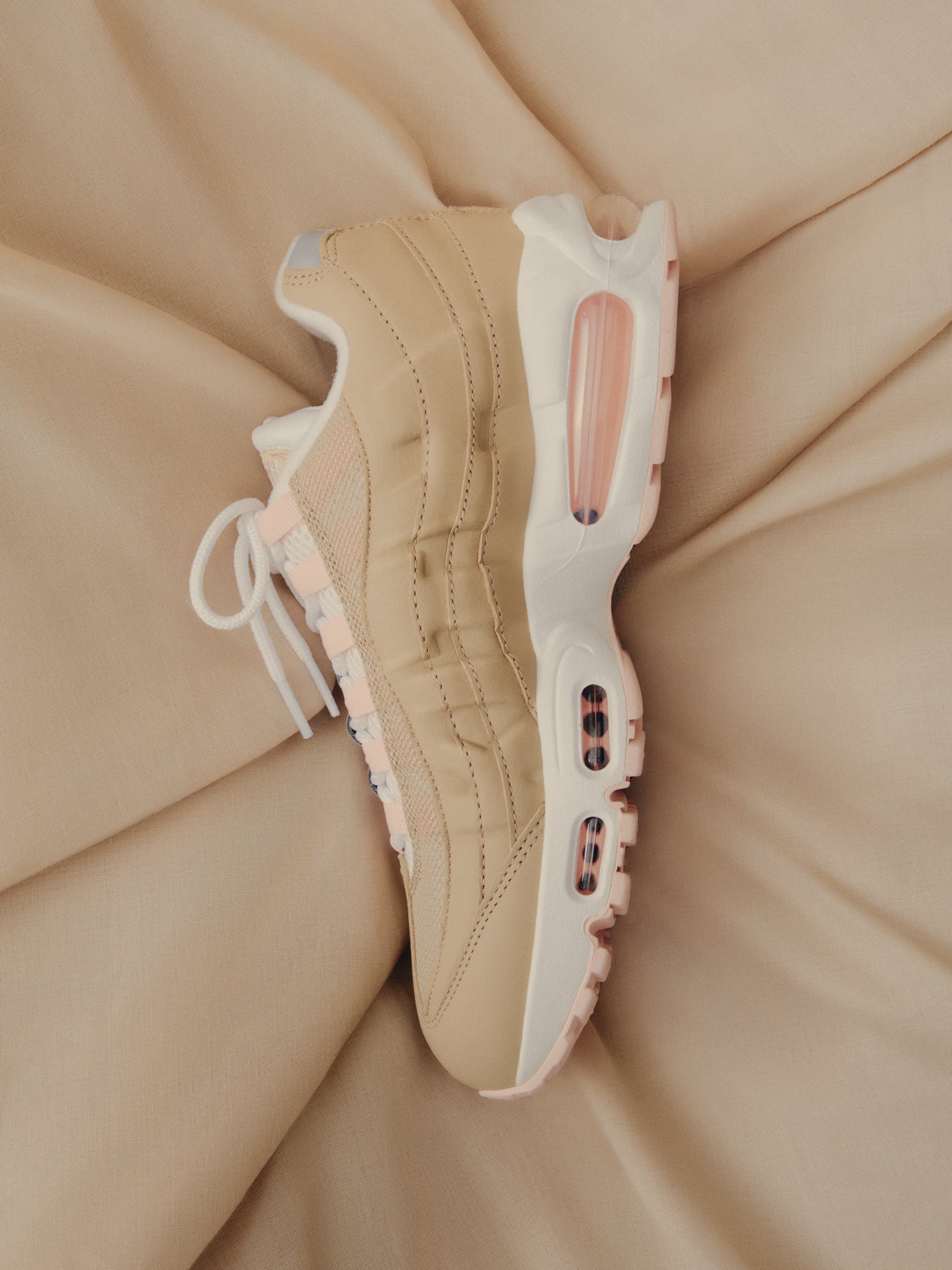 Nike Air Max 95 in tan and pink, top-down view resting on draped beige fabric at Kith