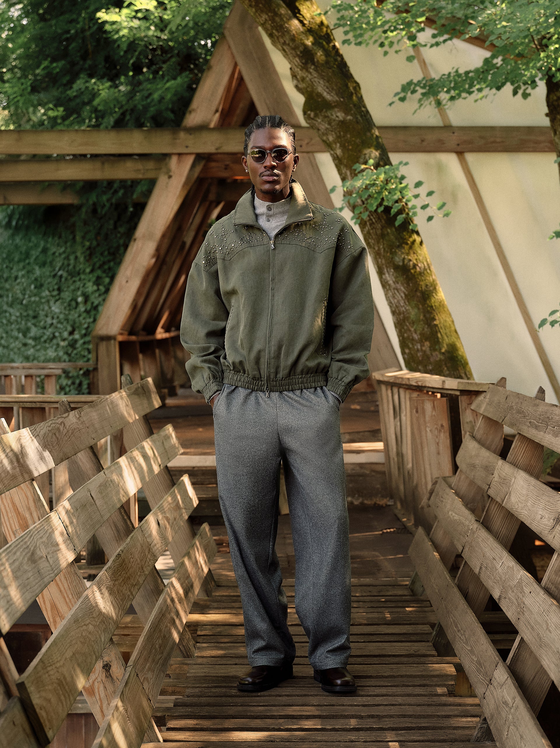Olive rhinestone-studded western zip jacket with grey trousers on model, full-length front view on wood bridge