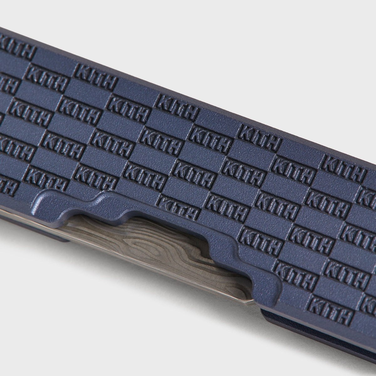 Macro detail of the KITH checkerboard engraving and damascus steel blade edge on the navy Yamori folding knife