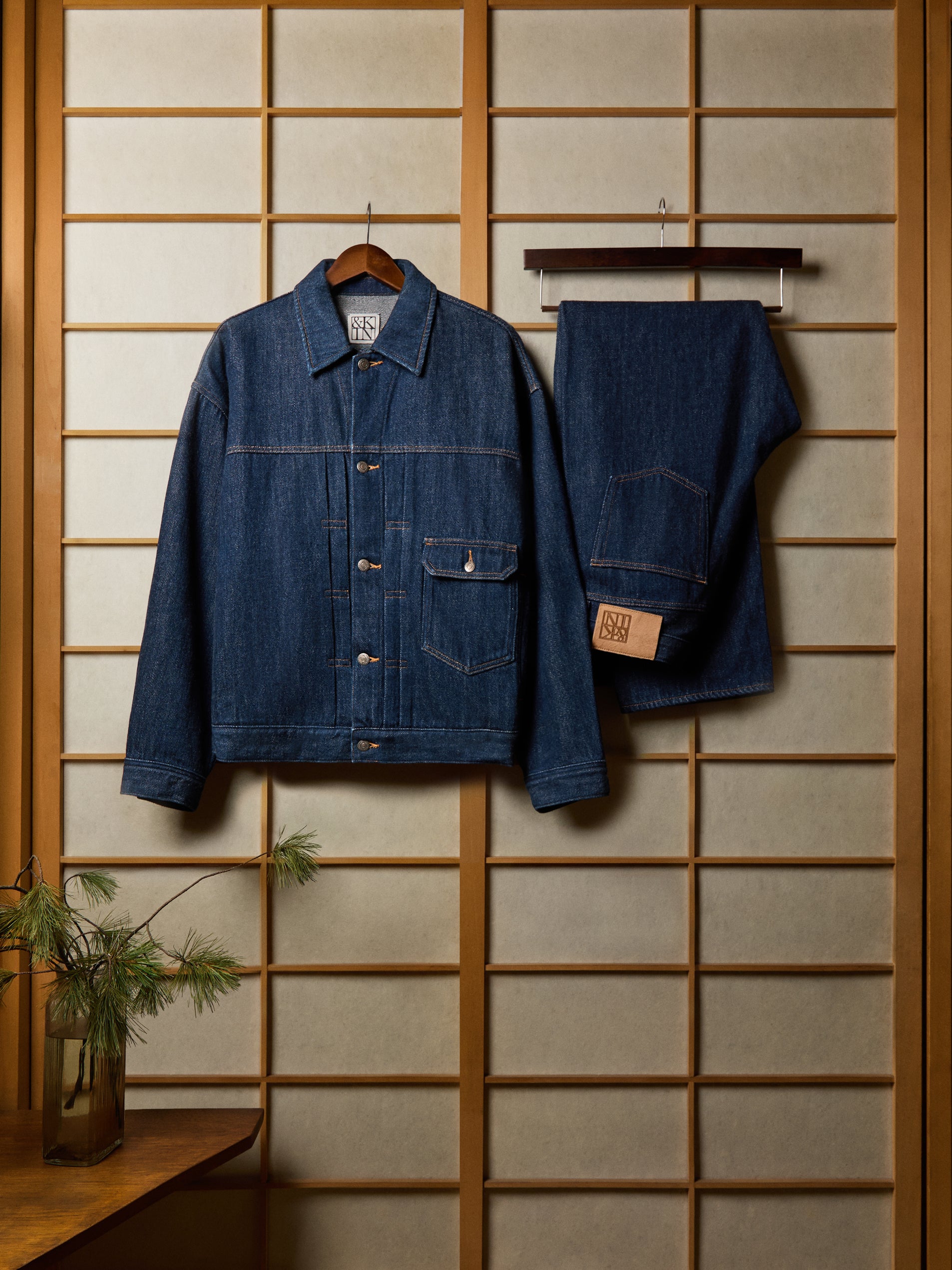 Indigo raw denim trucker jacket and matching jeans hung on wooden shoji screen, front view