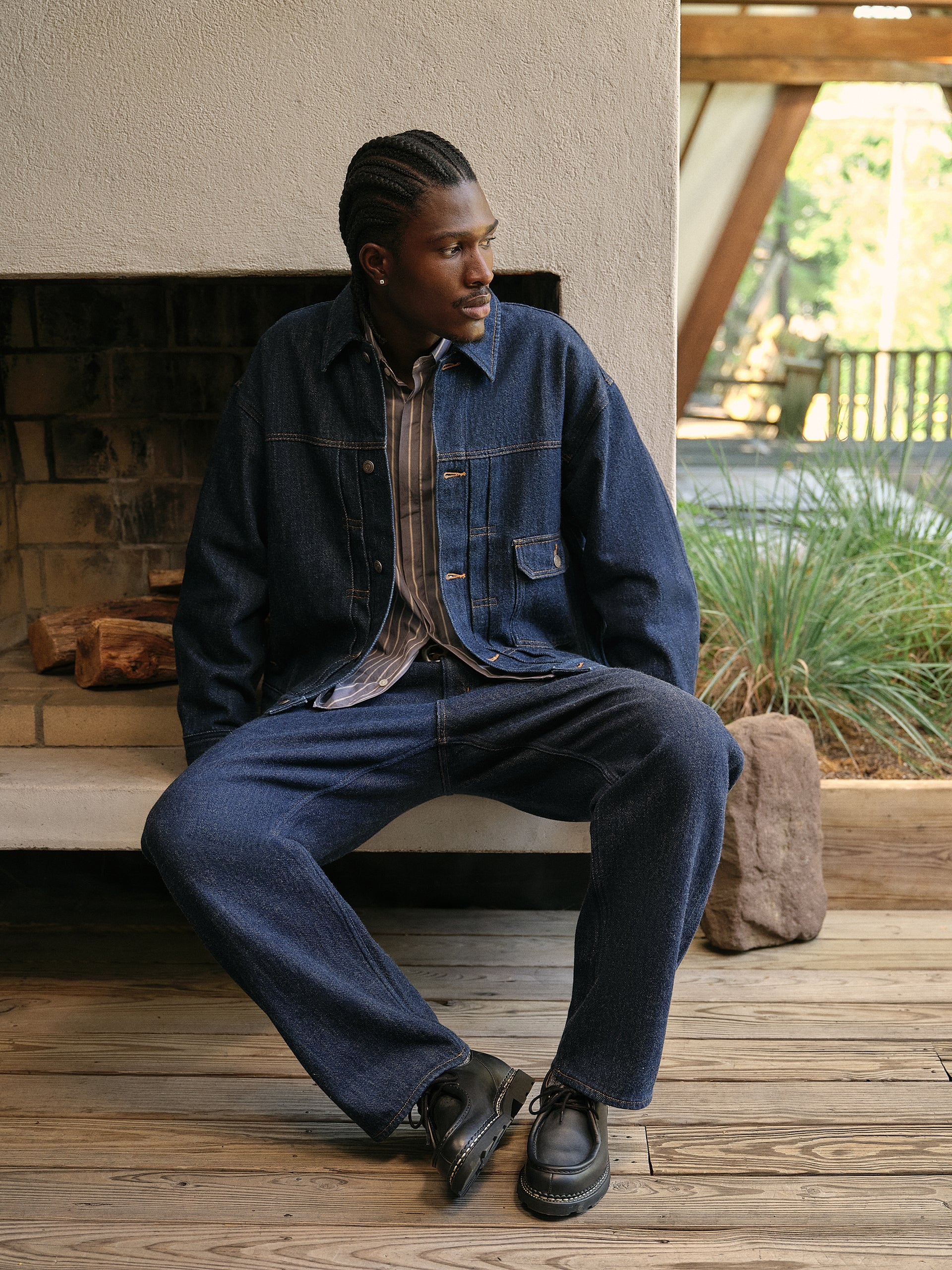 Distressed brown suede zip bomber jacket and taupe trousers on model leaning at wood A-frame stairs