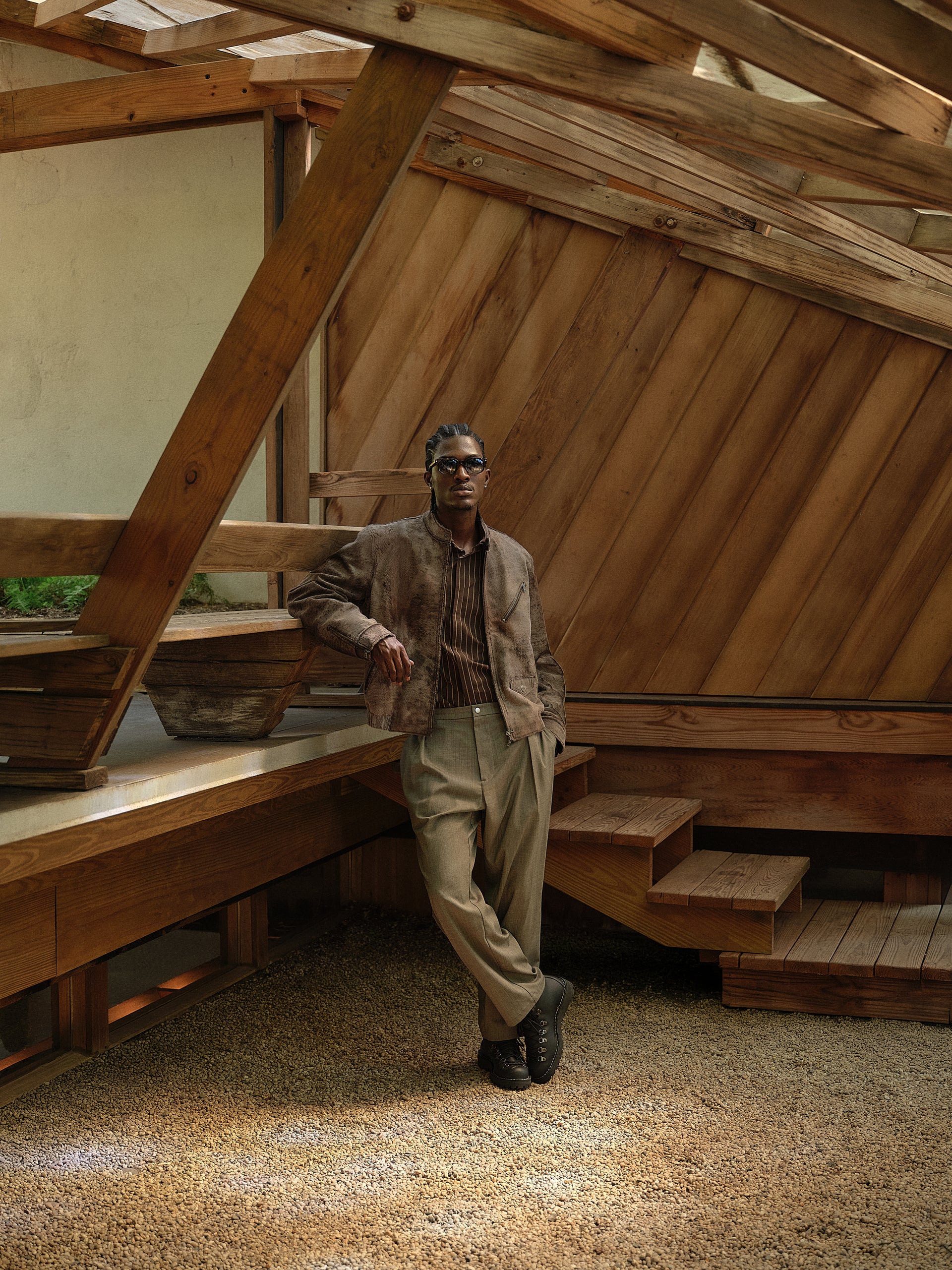 Indigo denim trucker jacket over striped shirt with wide jeans, model seated cross-legged by brick fireplace
