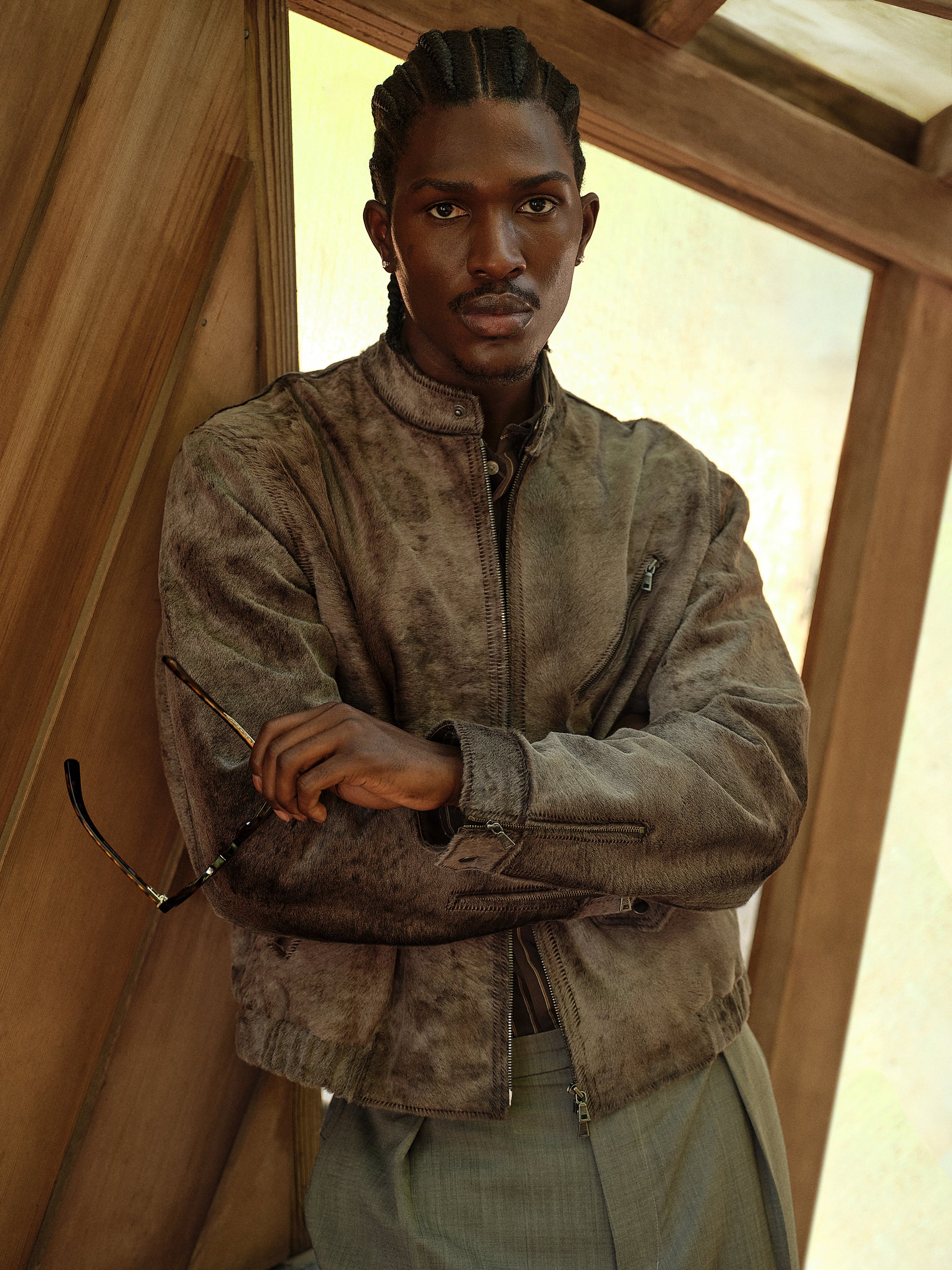 Distressed grey-brown suede zip jacket, model with arms crossed holding sunglasses, close front portrait