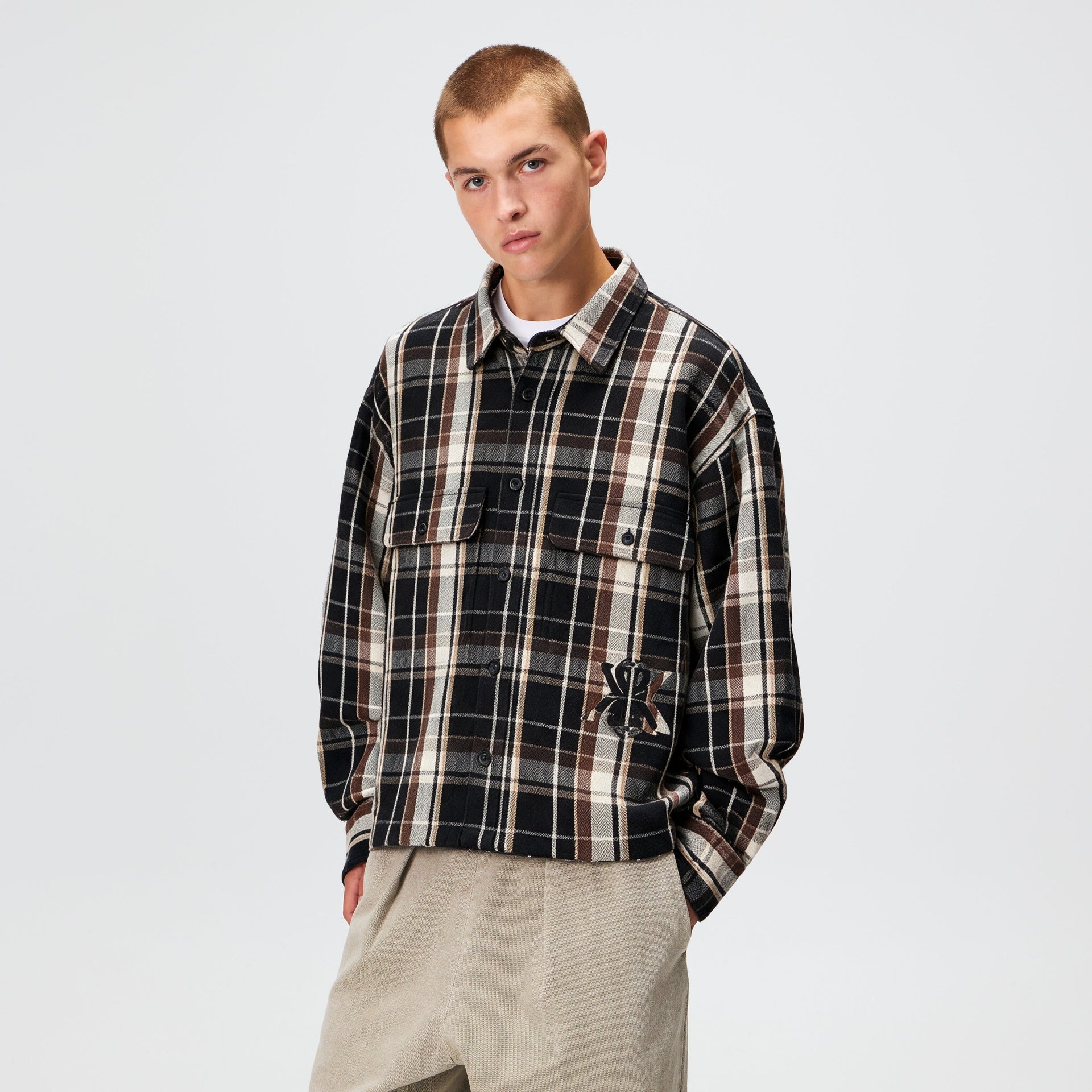 Man wearing the Kith Plaid Henson buttondown shirt in black plaid flannel with khaki trousers