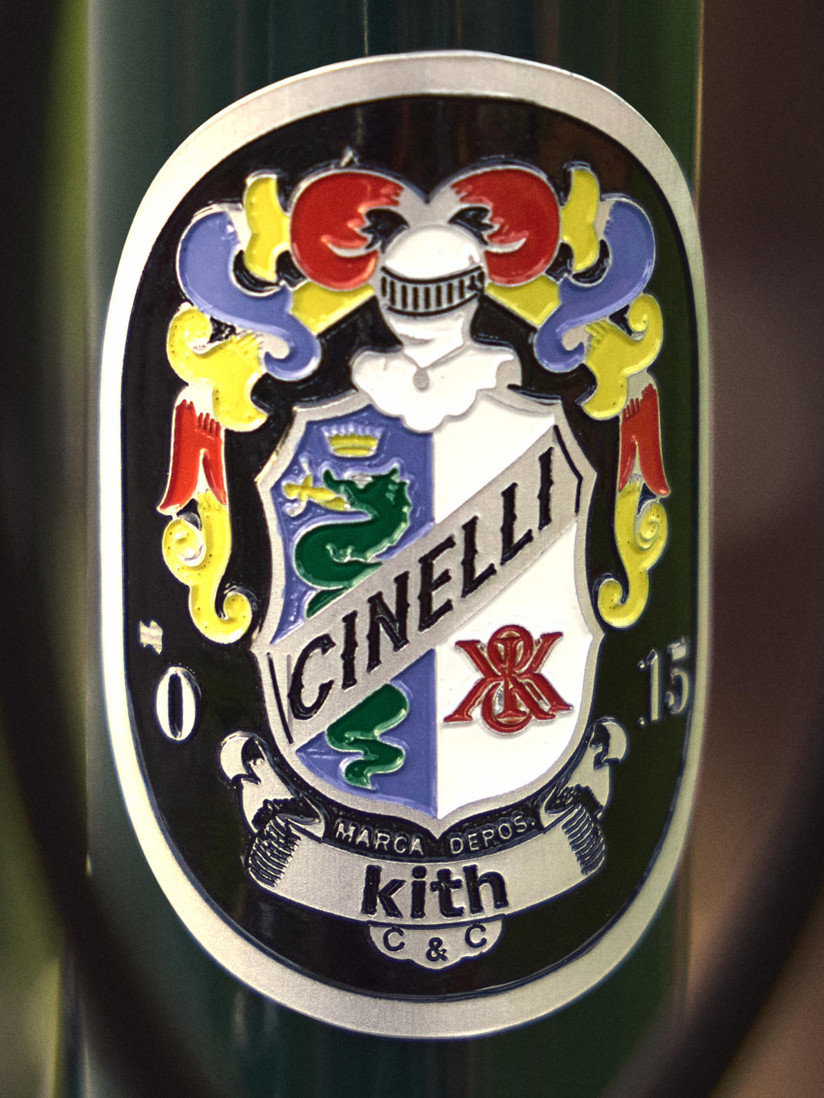 Macro of an enamel Cinelli head badge with a heraldic crest reading CINELLI and Kith C&C on a green bicycle frame