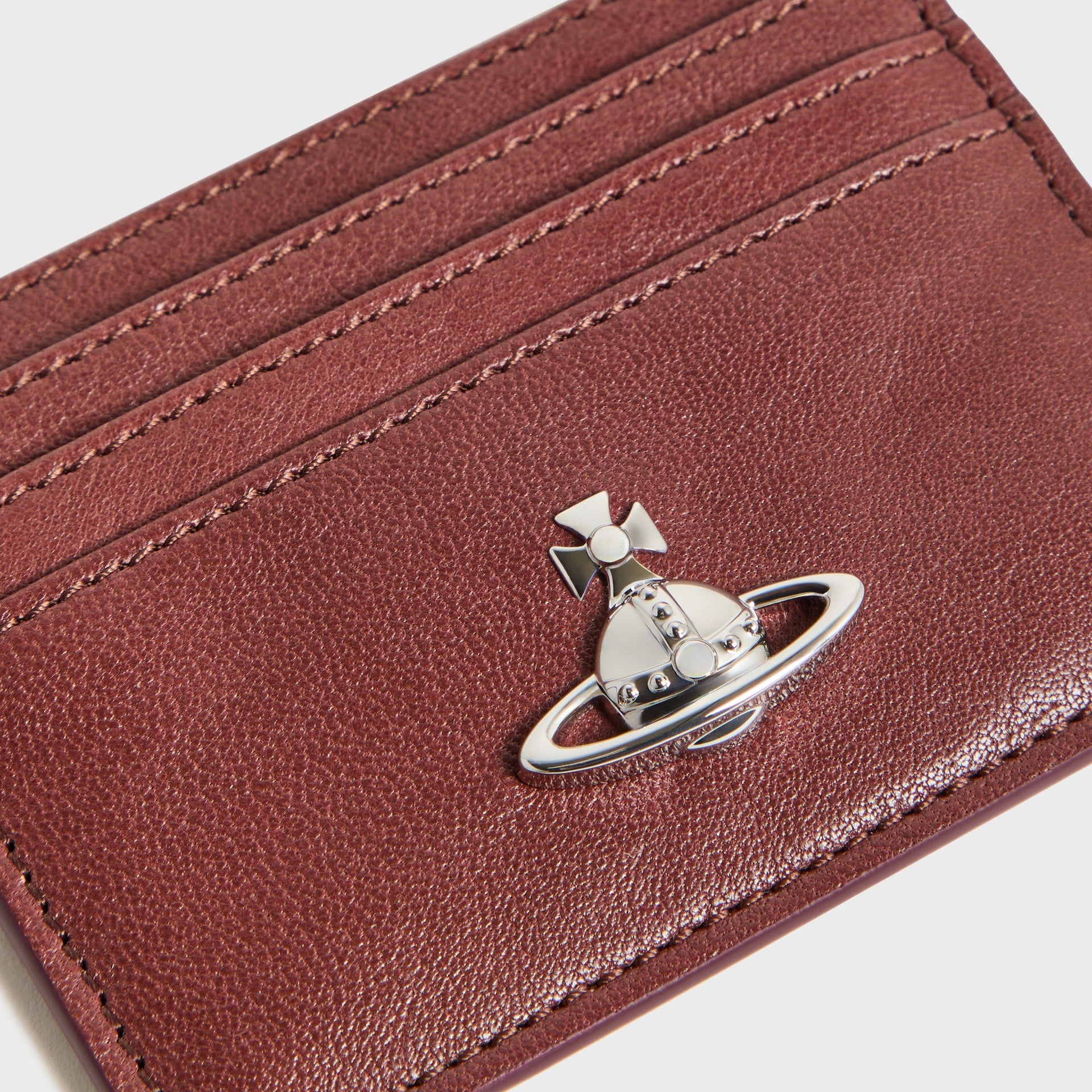 Vivienne Westwood chestnut card holder, angled close-up of silver Orb emblem on grained leather