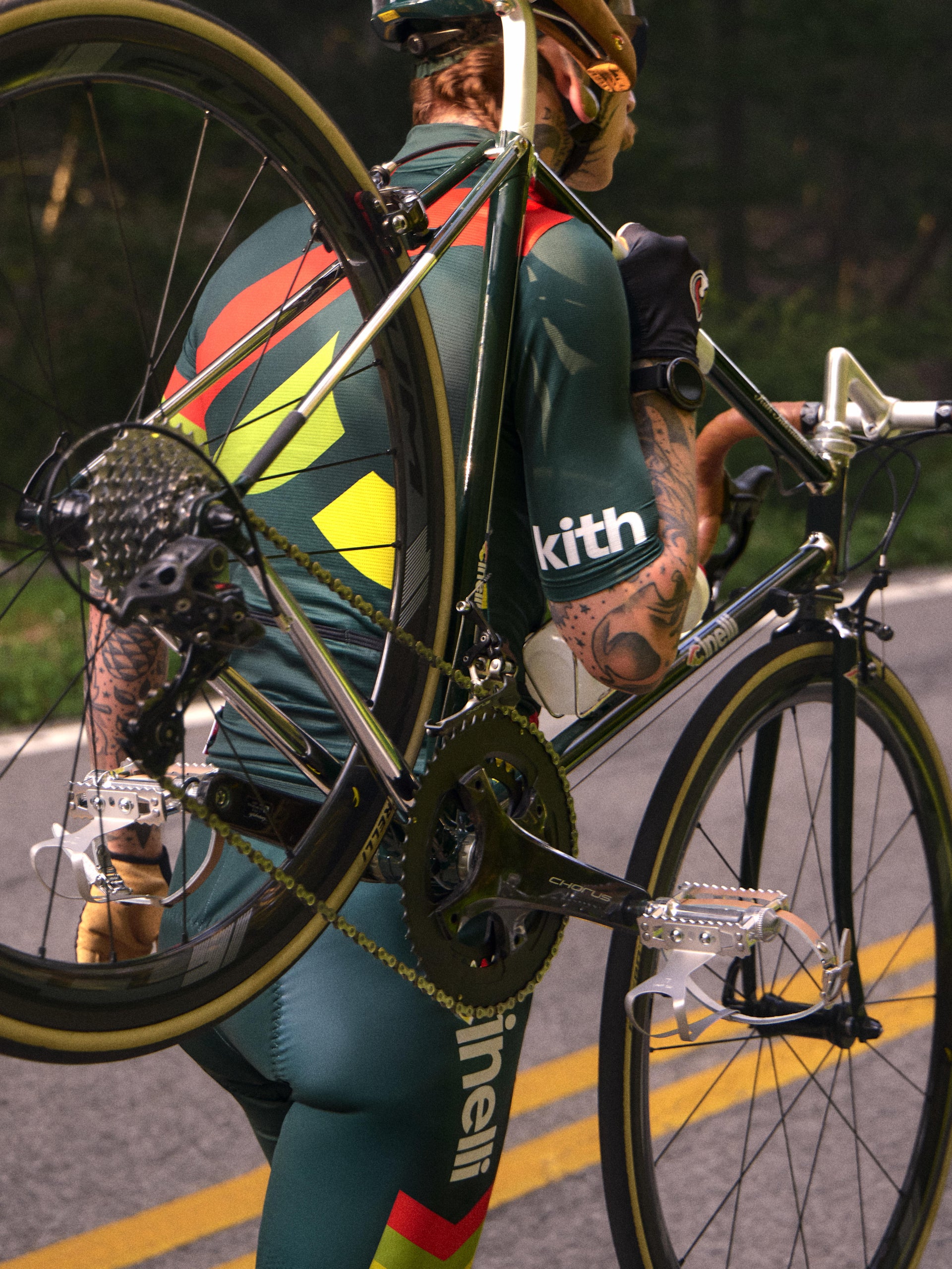 Cyclist in green Kith x Cinelli racing kit carrying a green Cinelli road bike over the shoulder, back view
