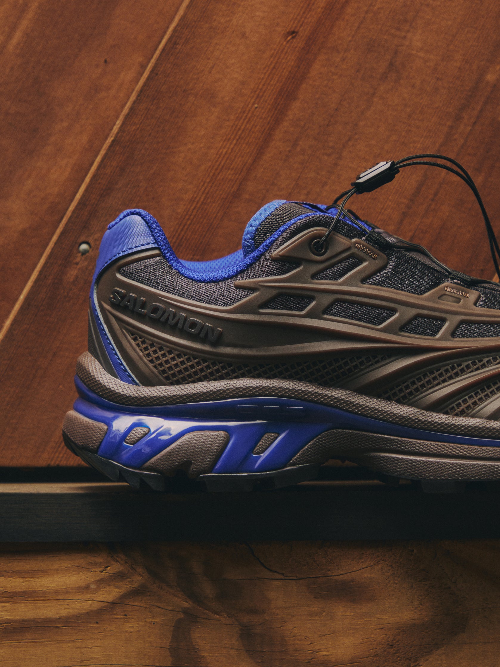 Salomon XT-6 sneaker in brown and blue, side profile with quicklace on warm wood