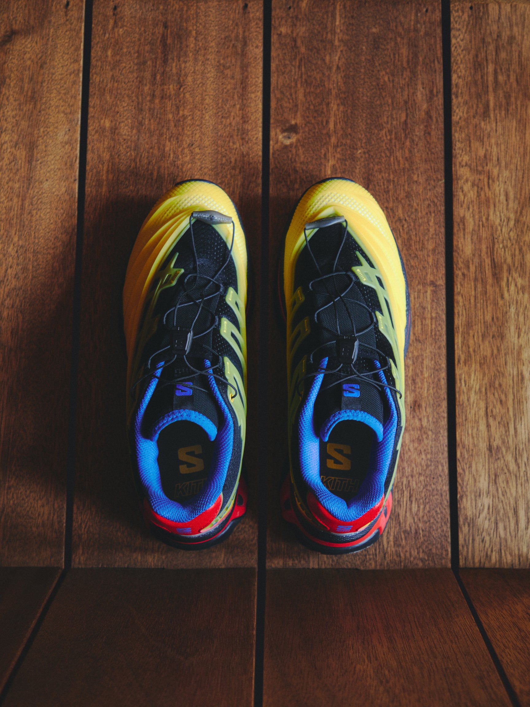 Salomon XT-6 sneakers in black, yellow, blue and red, top-down view on wood planks