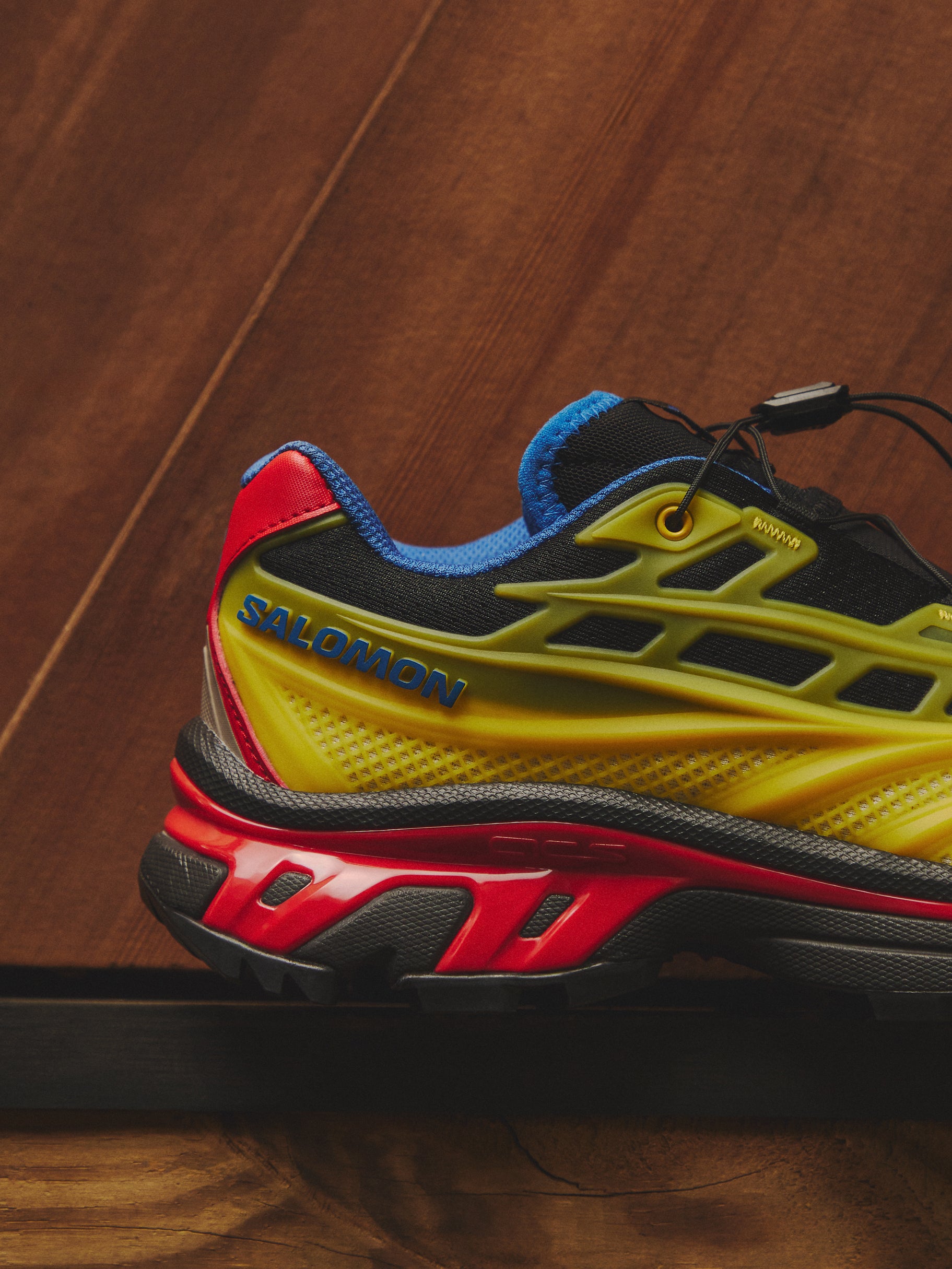 Salomon XT-6 sneaker in yellow, red and blue, heel and midsole detail on dark wood