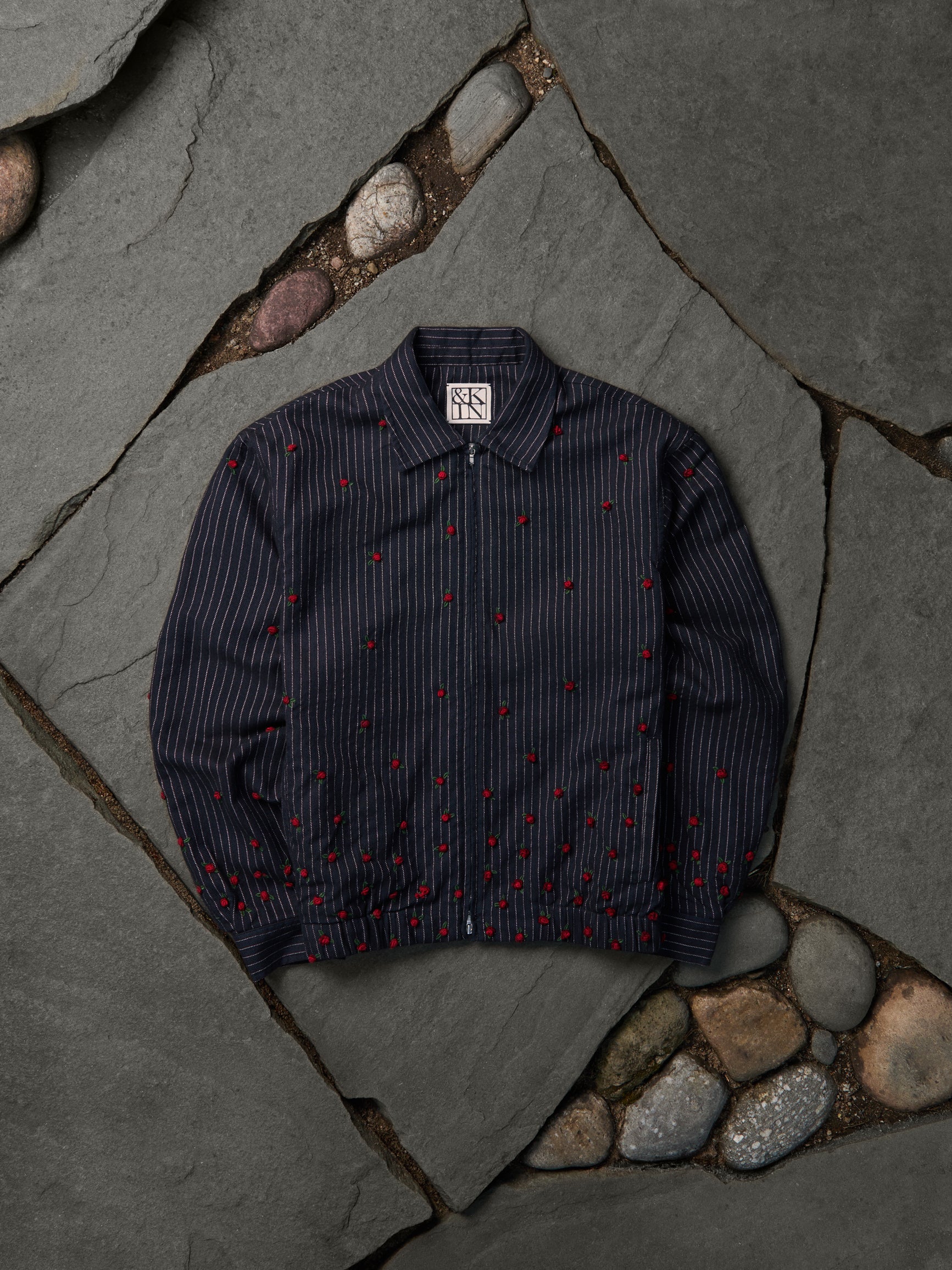 KIN navy pinstripe jacket with red rose embroidery, flat-lay on slate flagstones