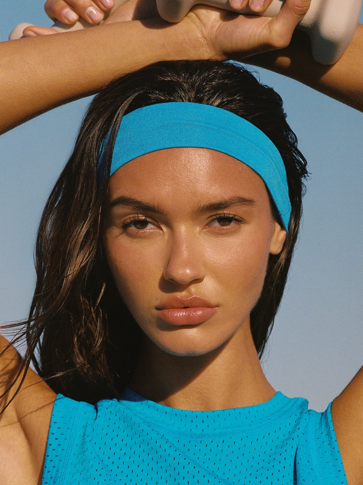 Model in blue Kith mesh tank top and turquoise athletic headband against a blue sky