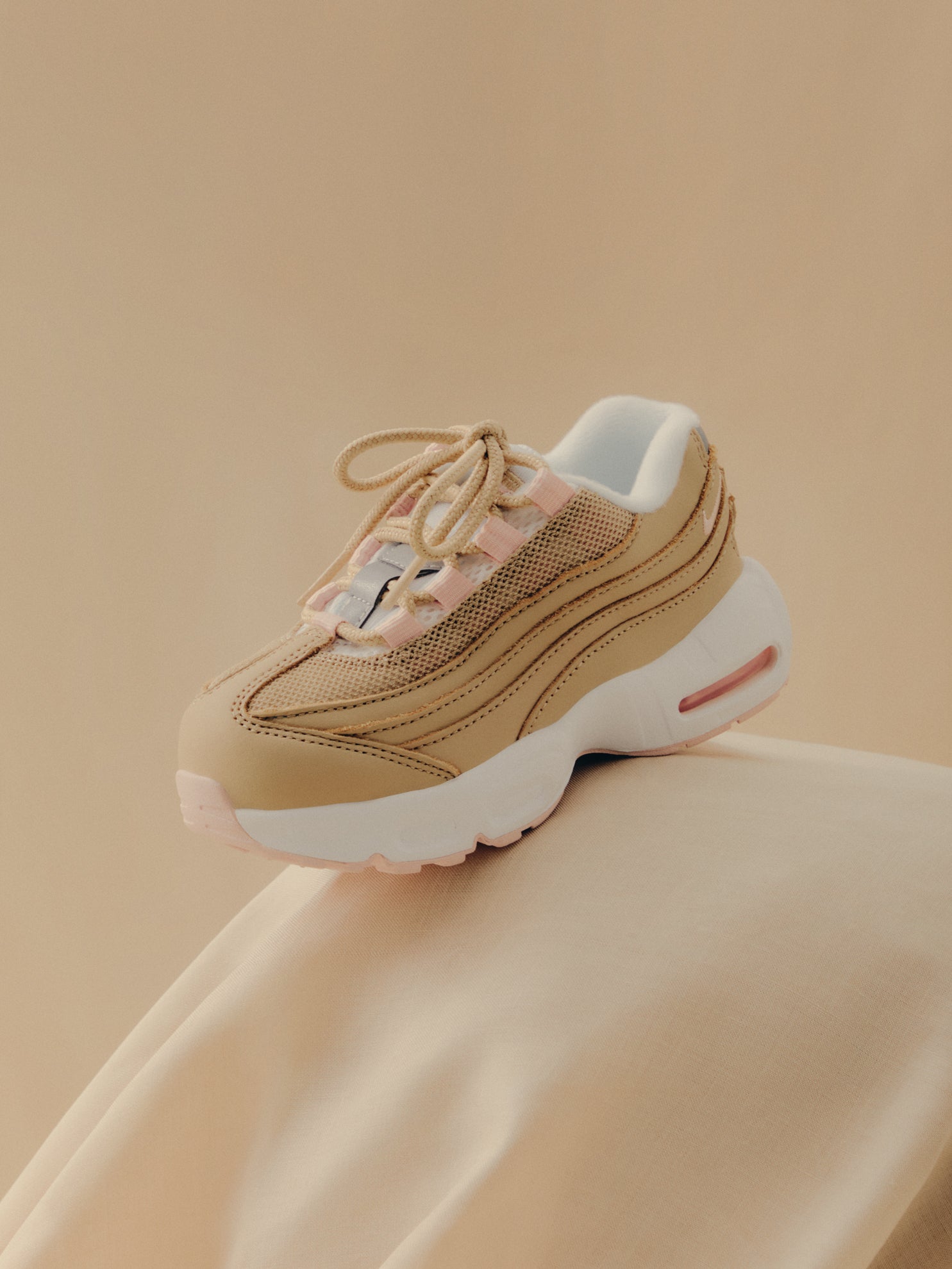 Nike Air Max 95 sneaker in tan and pink perched on cream fabric, side view, Kith