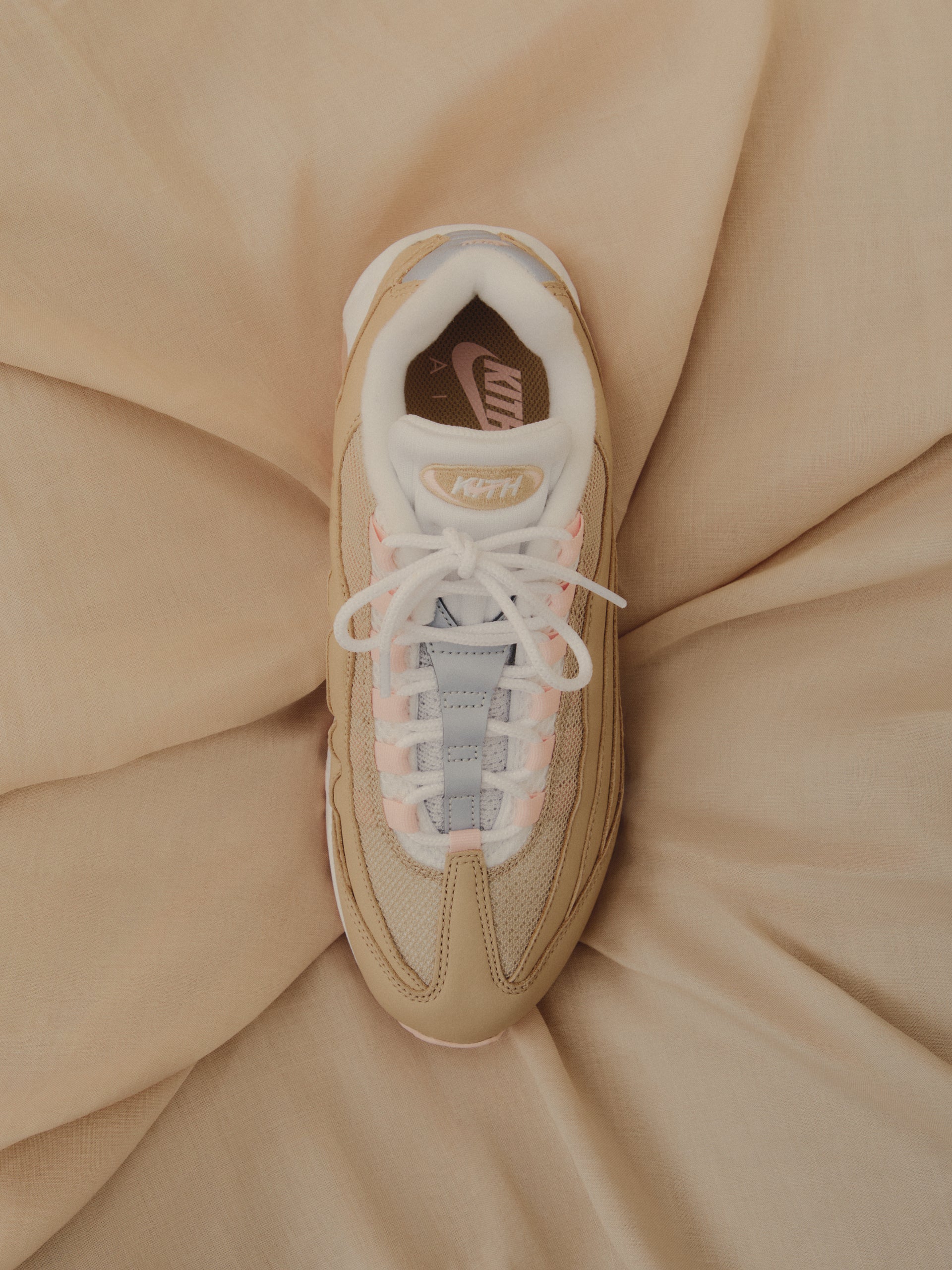Top-down view of tan Nike Air Max 95 x Kith sneaker with pink accents on beige fabric