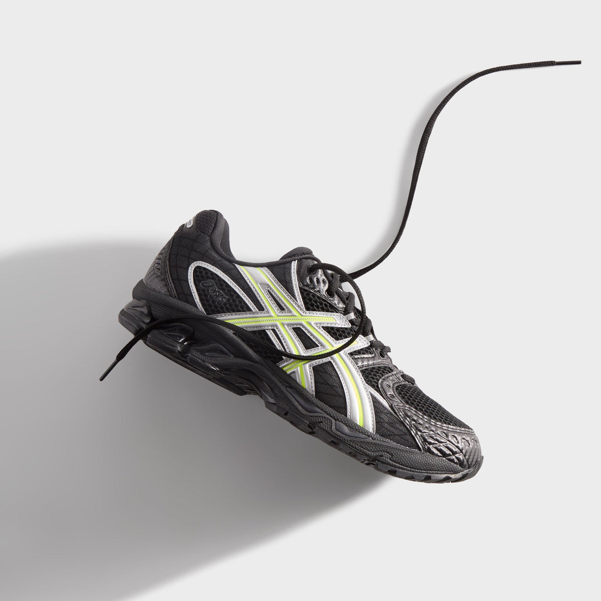Kith for ASICS GEL-NIMBUS 10.1 black and silver, single shoe tilted in mid-air with long lace trailing and soft shadow