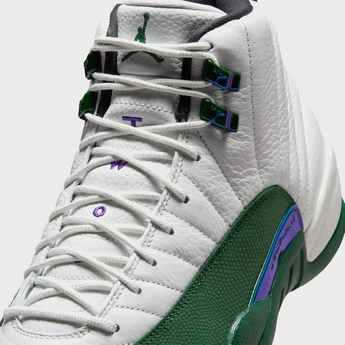Close-up of Air Jordan 12 Retro lace eyelets showing iridescent green Jumpman lace locks on white ribbed leather