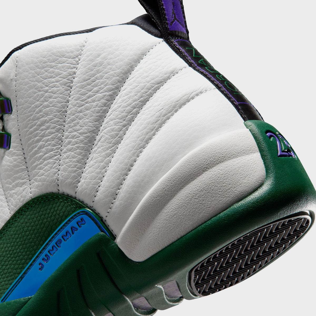 Close-up of Air Jordan 12 Retro heel and outsole edge showing holographic Jumpman script on the green mudguard