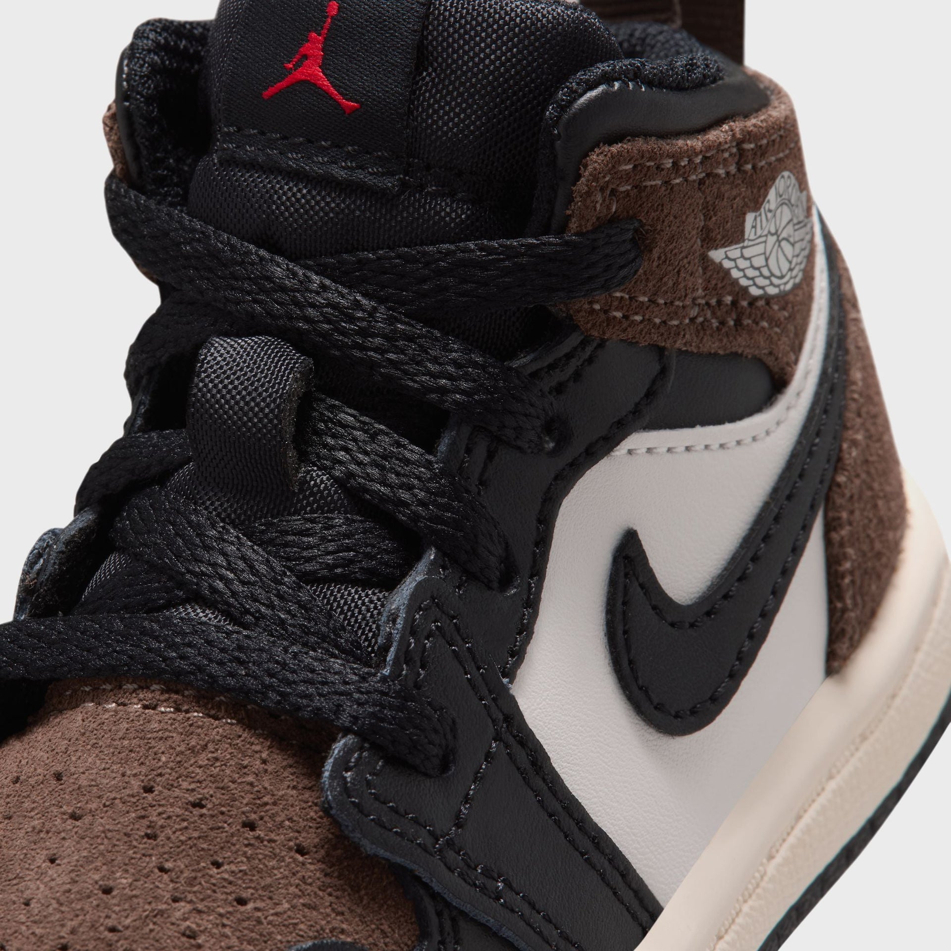 Jordan 1 Mid toddler close-up of brown suede overlay, black Swoosh on phantom leather and red Jumpman tongue