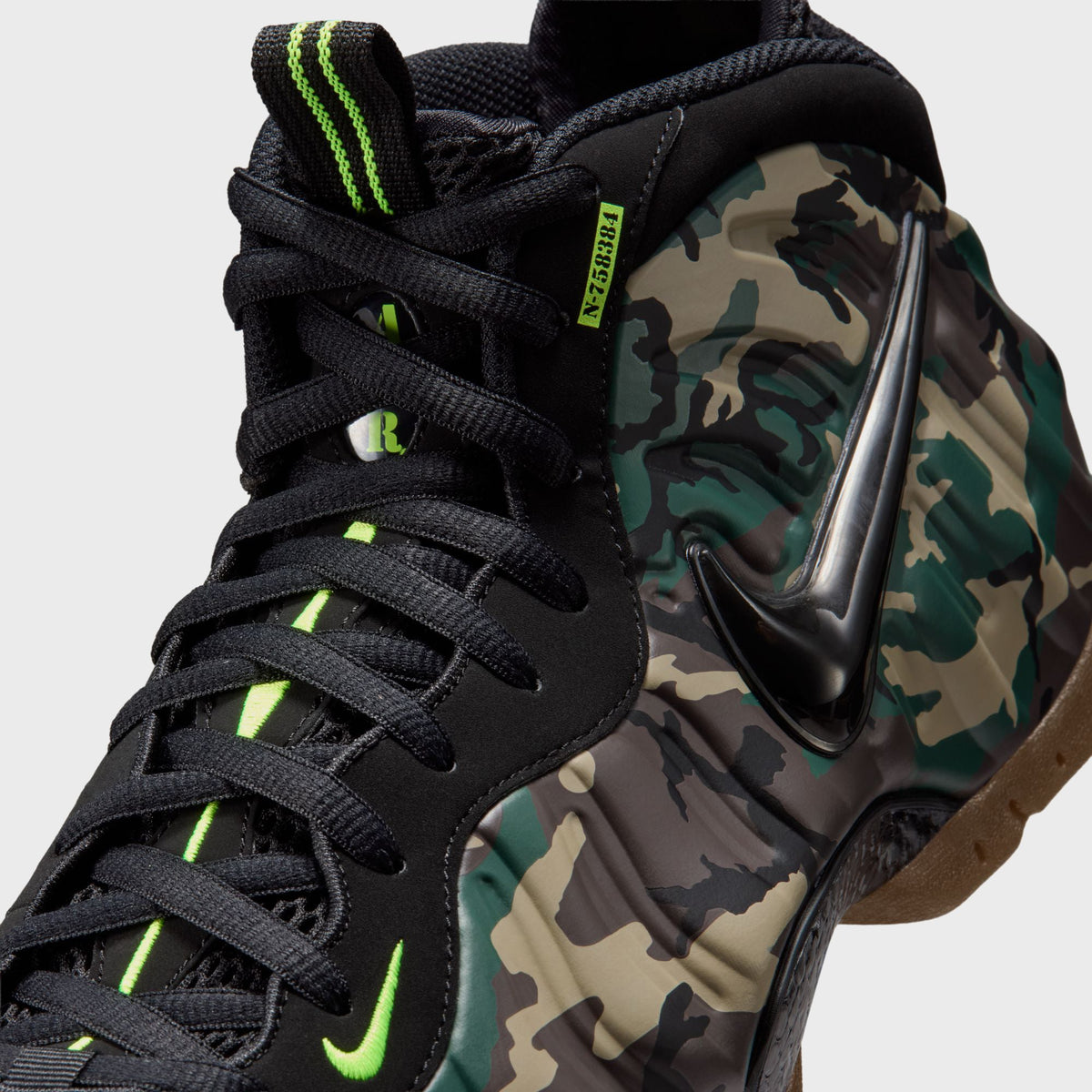 Close-up of Nike Air Foamposite Pro toe featuring glossy black Swoosh overlay on green and tan camo foam