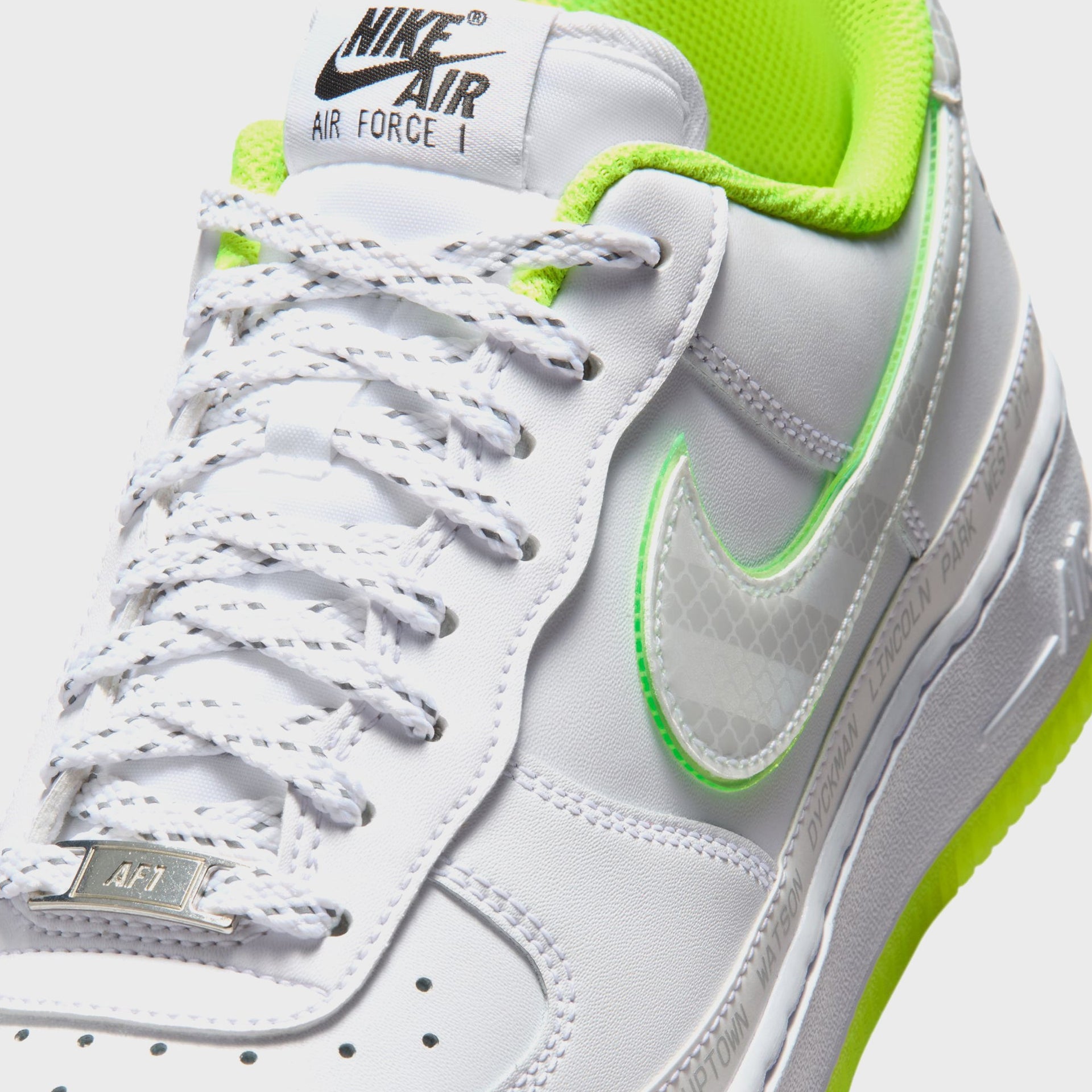 Nike Air Force 1 '07 forefoot close-up: white leather, silver AF1 dubrae and a translucent grid Swoosh with green trim over a volt sole