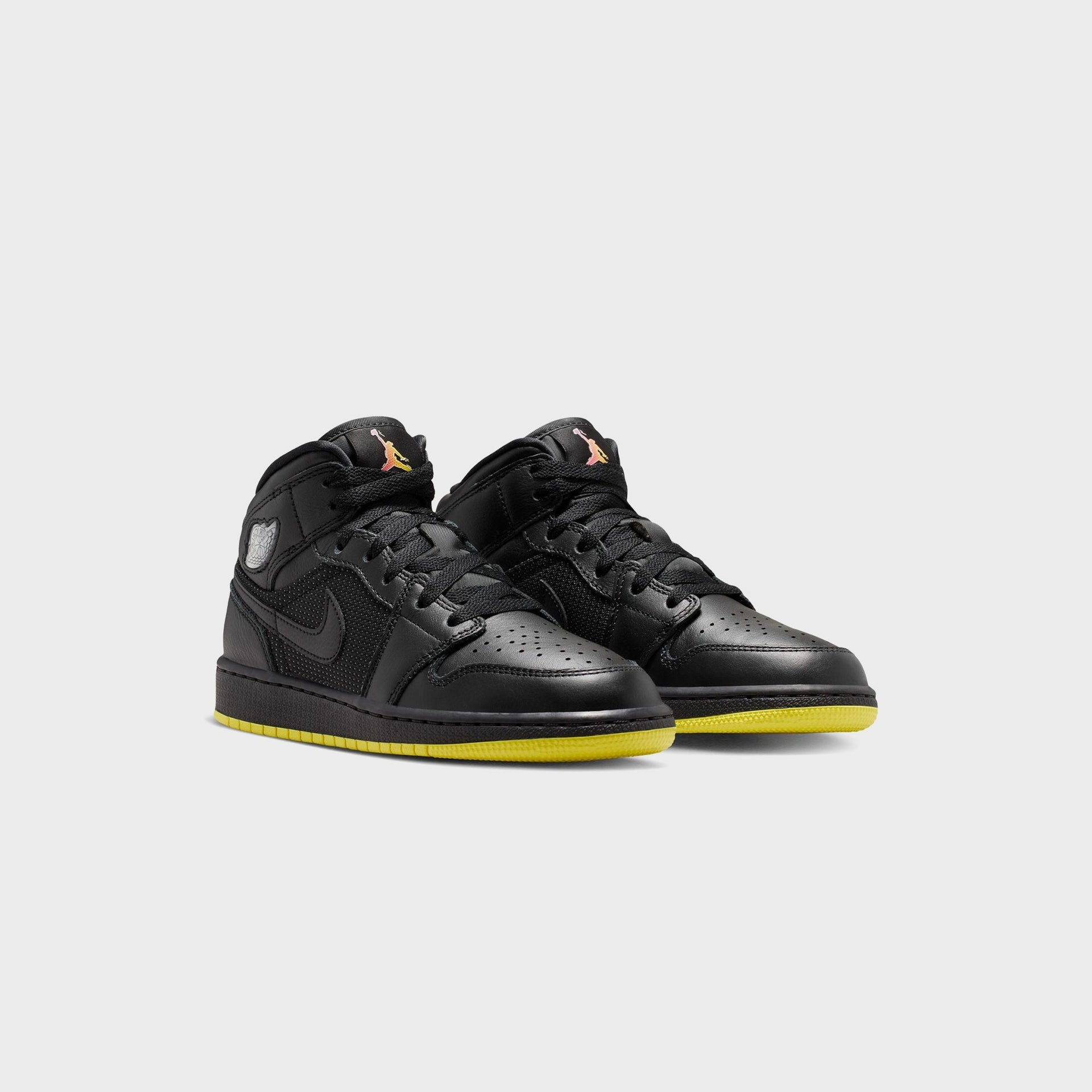 Air Jordan 1 Mid SE pair, front three-quarter view showing black uppers, gradient Jumpman tongues and opti yellow outsoles