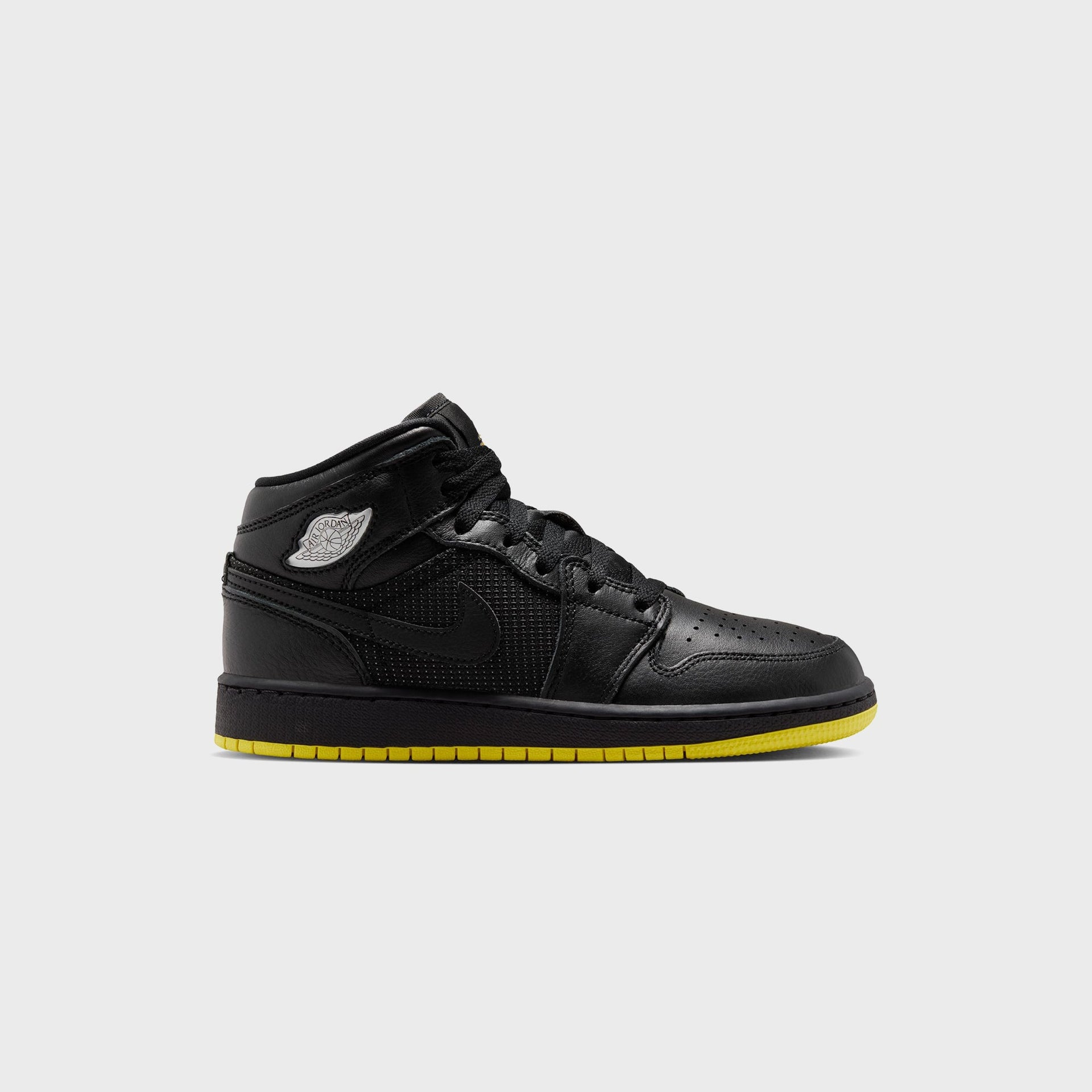 Air Jordan 1 Mid SE in black leather with perforated panel and silver Wings logo, lateral side view over an opti yellow outsole