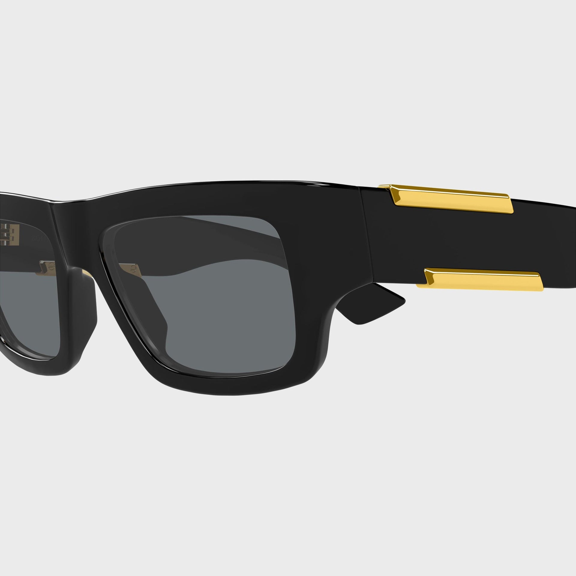 Bottega Veneta Dash rectangular sunglasses, close-up of black frame corner, grey lens and gold temple bars
