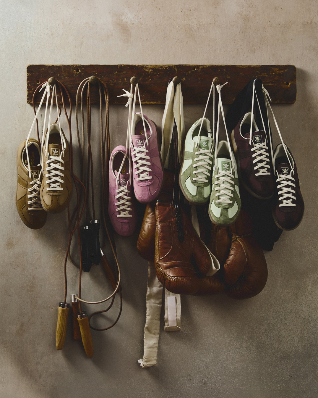Kith for adidas suede sneakers in tan, pink, green and burgundy hung on a rack beside vintage boxing gloves