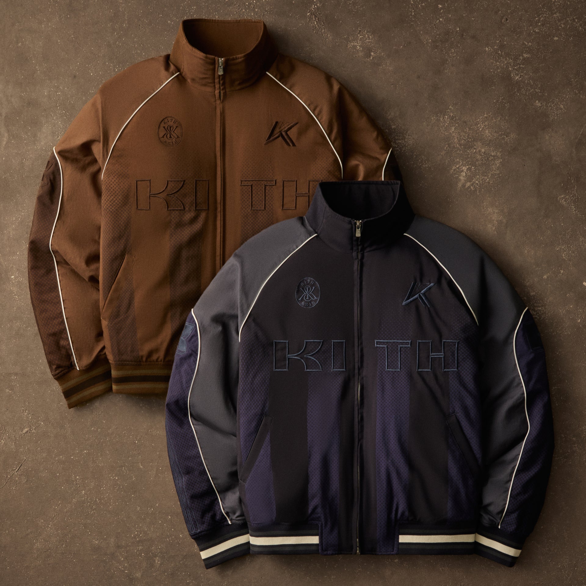 Brown and navy Kith varsity jackets with embroidered logo detailing layered together against a brown backdrop