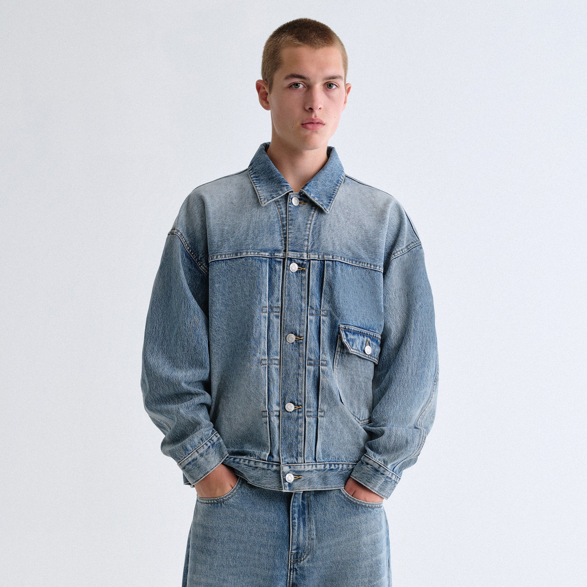 Man wearing a light blue Kith denim trucker jacket and matching jeans against a grey backdrop
