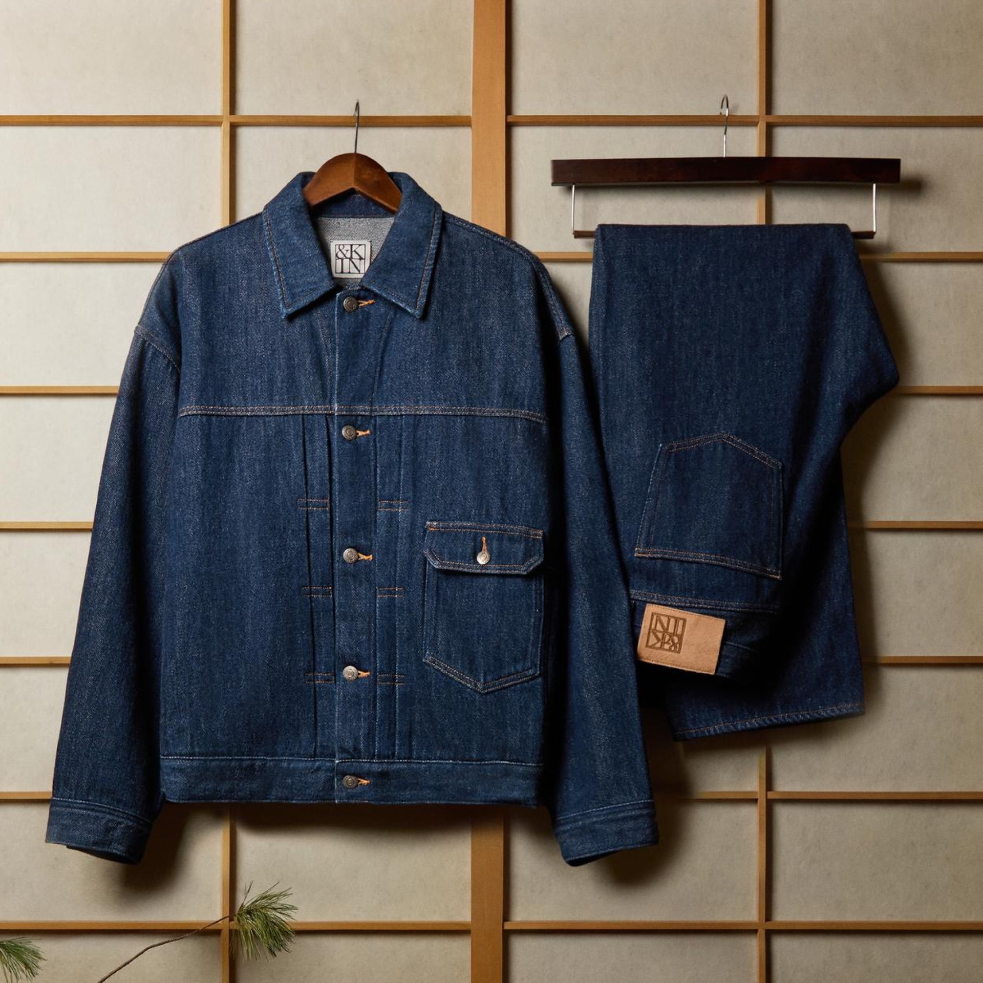 Indigo raw denim Kith trucker jacket and jeans hanging on a wooden hanger against a shoji screen backdrop