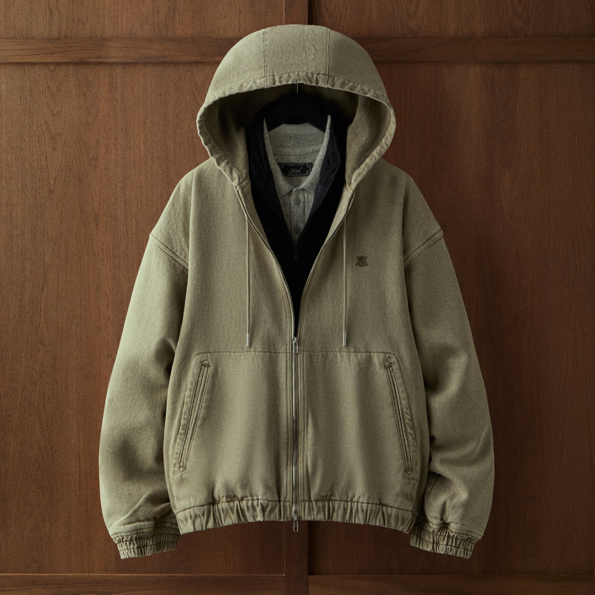 Olive green Kith hooded jacket with fleece-lined hood against a dark wood paneled background