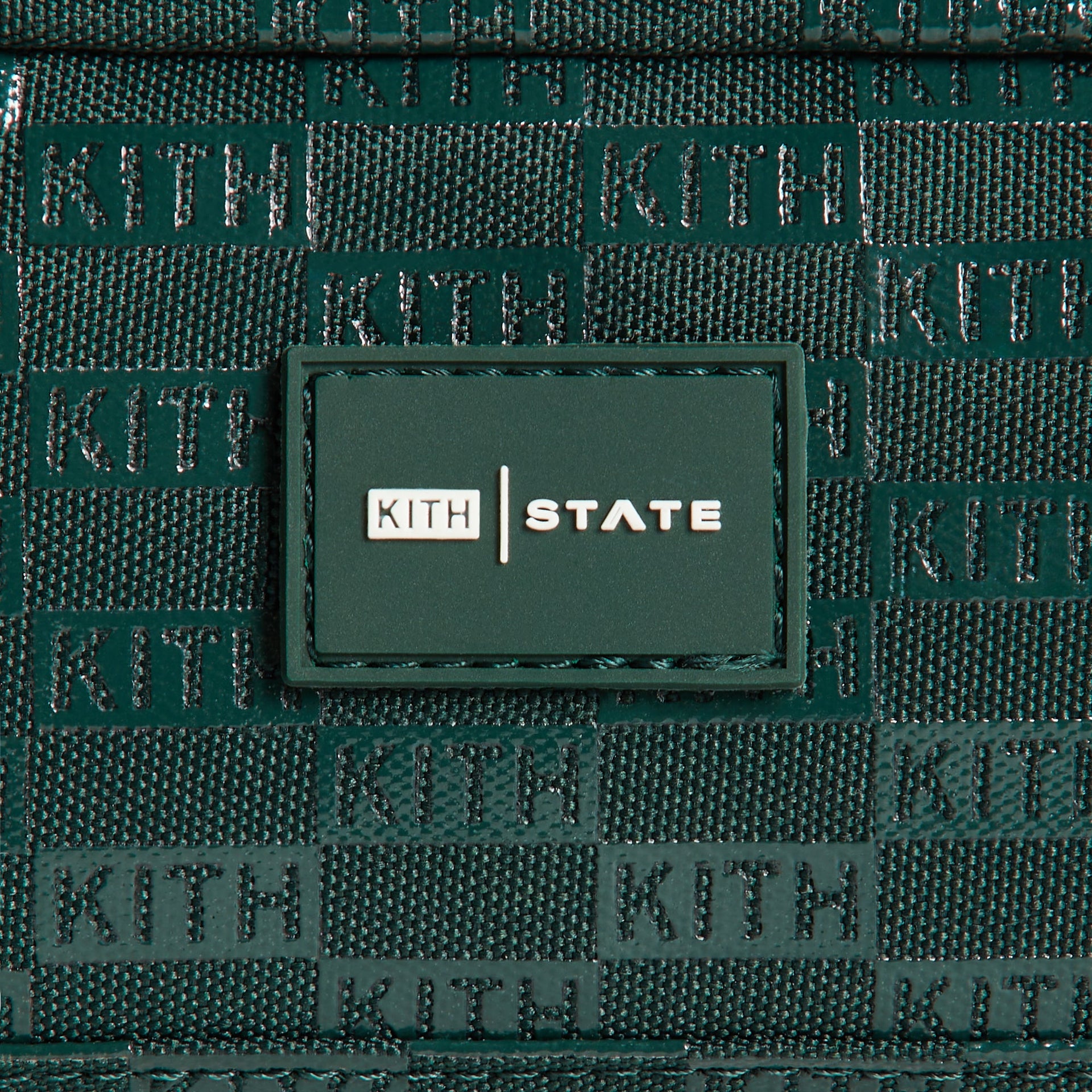 Kith Kids for STATE Clinton Pencil Case, close-up of KITH STATE rubber logo patch on green monogram fabric