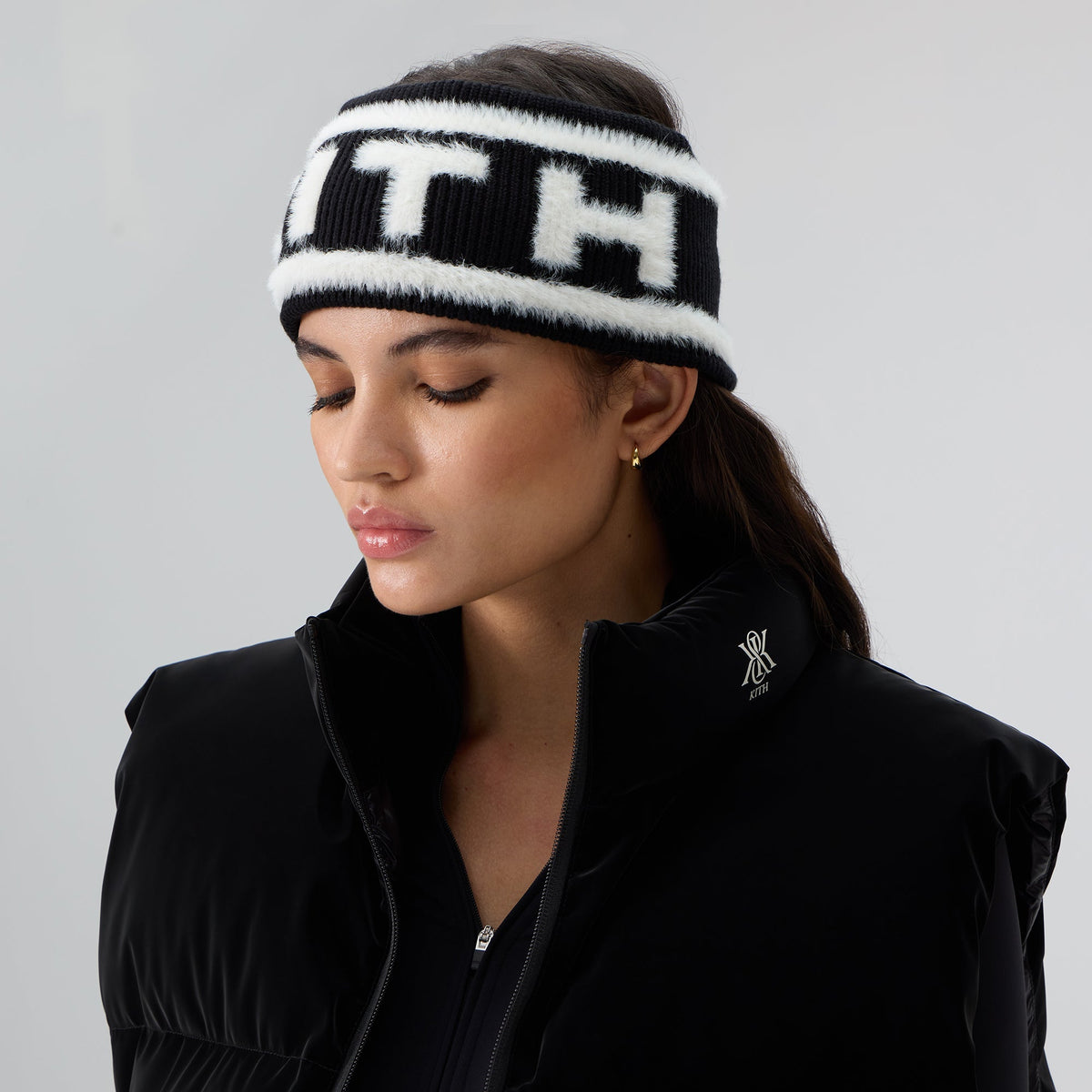 Model wearing the black Kith Jacquard Rib Headband with white 'KITH' logo, side angle with black zip jacket and gold earrings